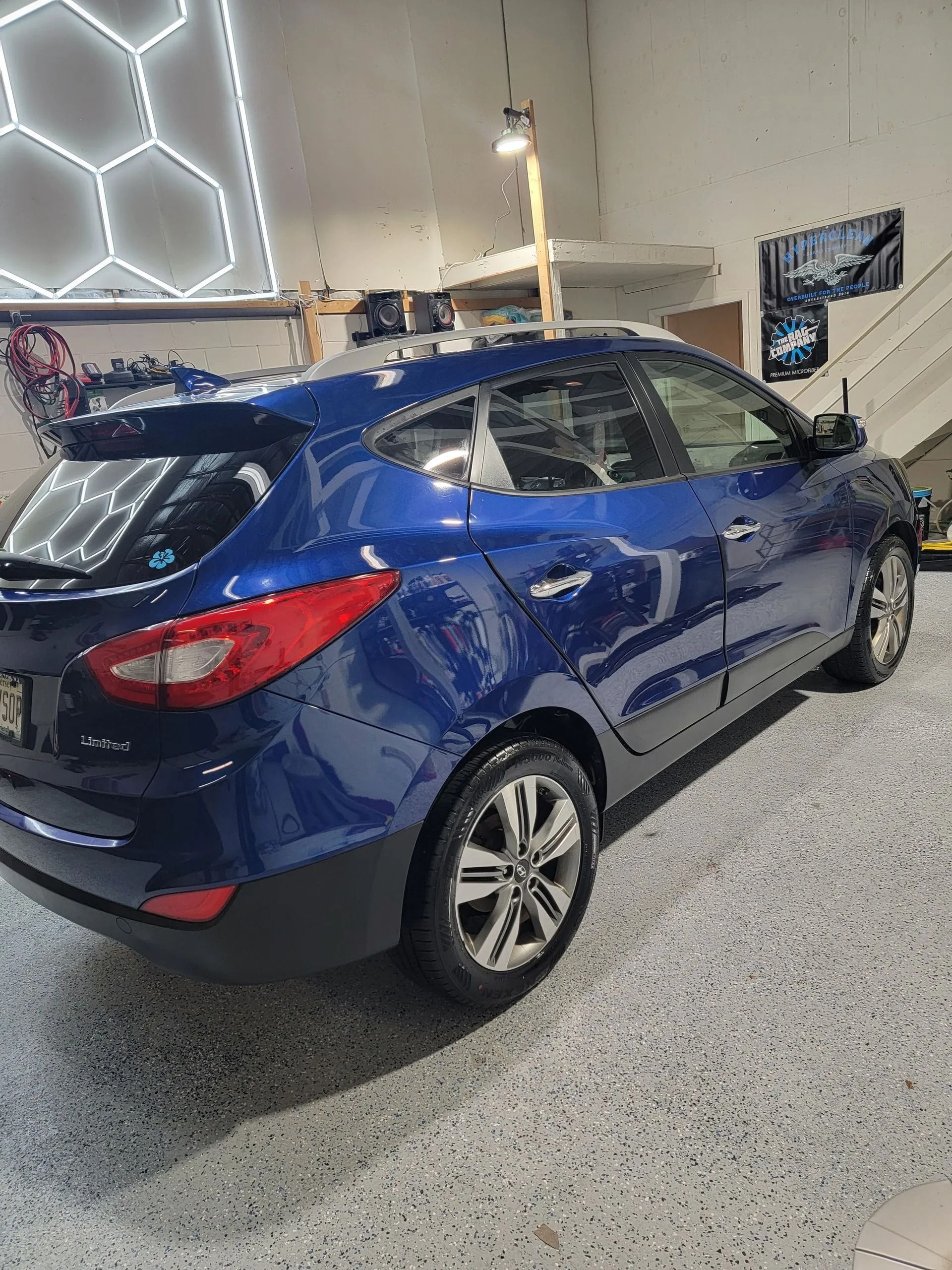 A blue SUV parked in a garage with a geometric-patterned ceiling light and a speckled floor.