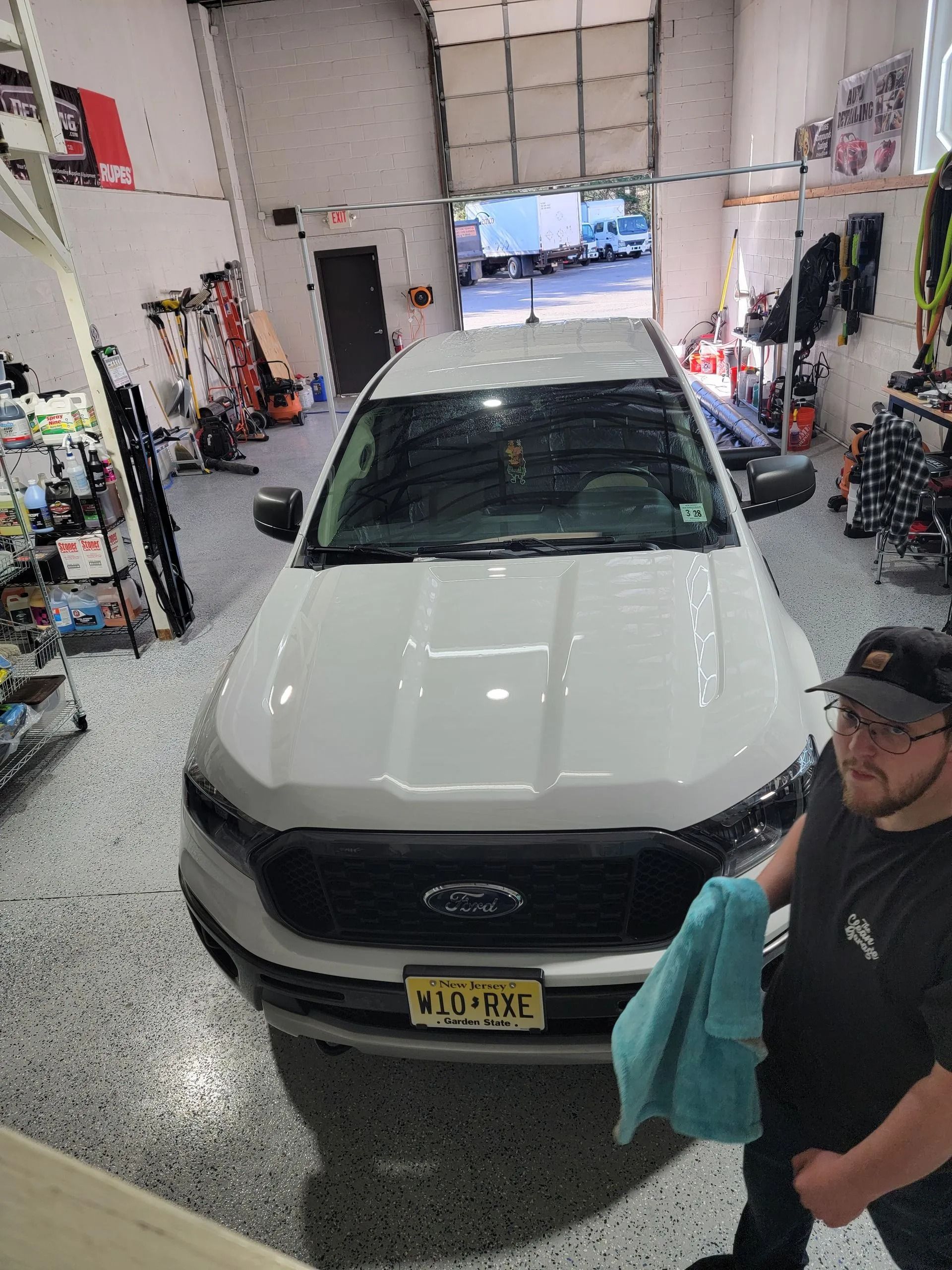 A man holding a blue towel stands next to a clean white Ford pickup truck inside a garage.