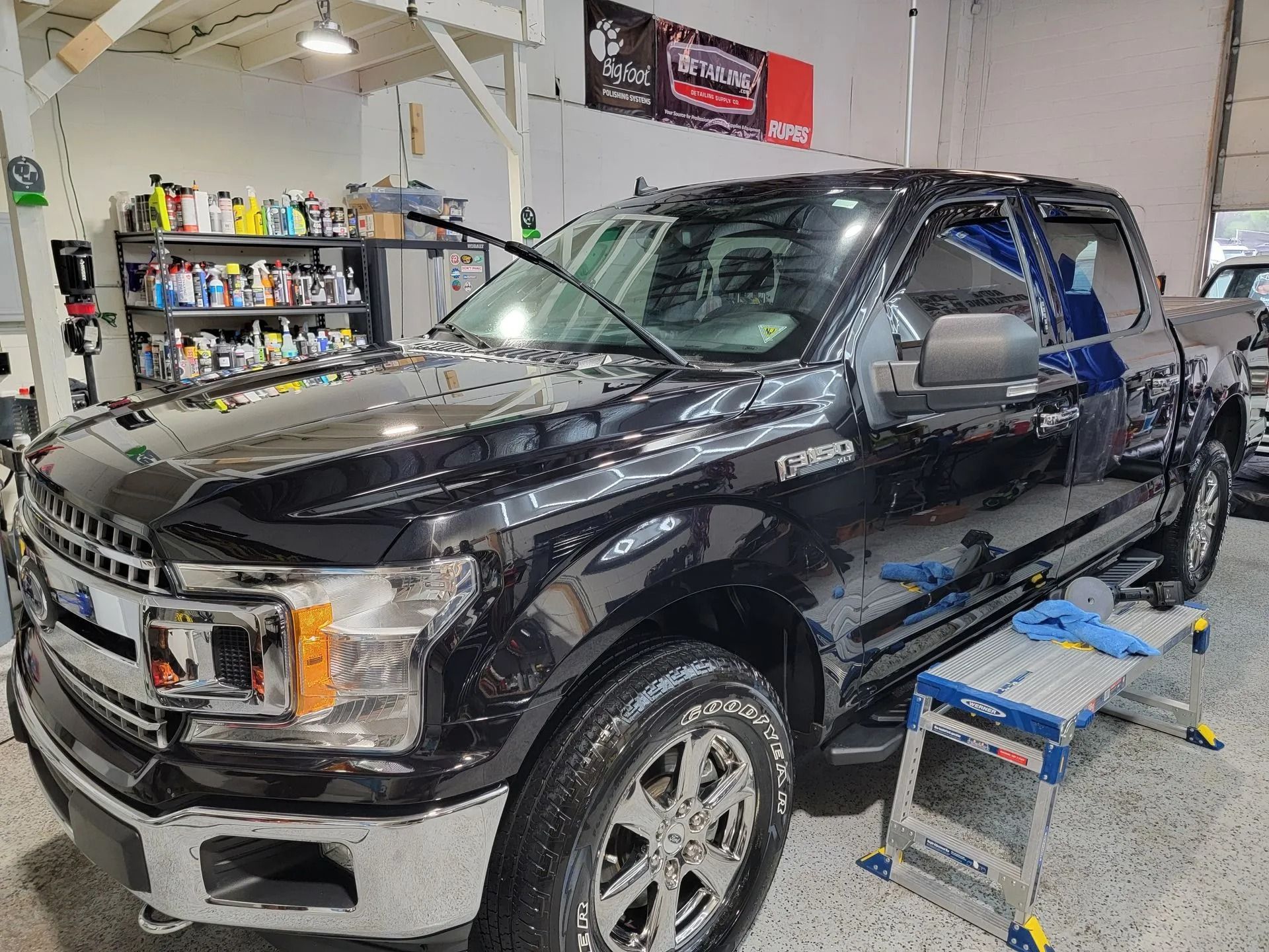 A black Ford F-150 truck parked in a garage with a step stool beside it.