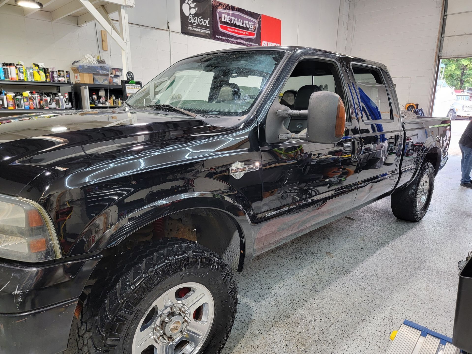 A black Ford Super Duty pickup truck parked inside a bright, well-lit workshop with organized shelves in the background.
