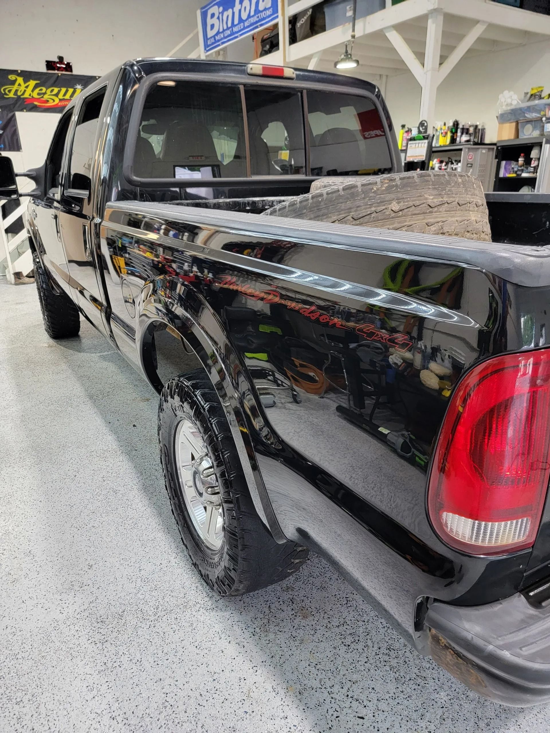 A black Ford F-Series pickup truck parked inside a garage with a speckled floor.