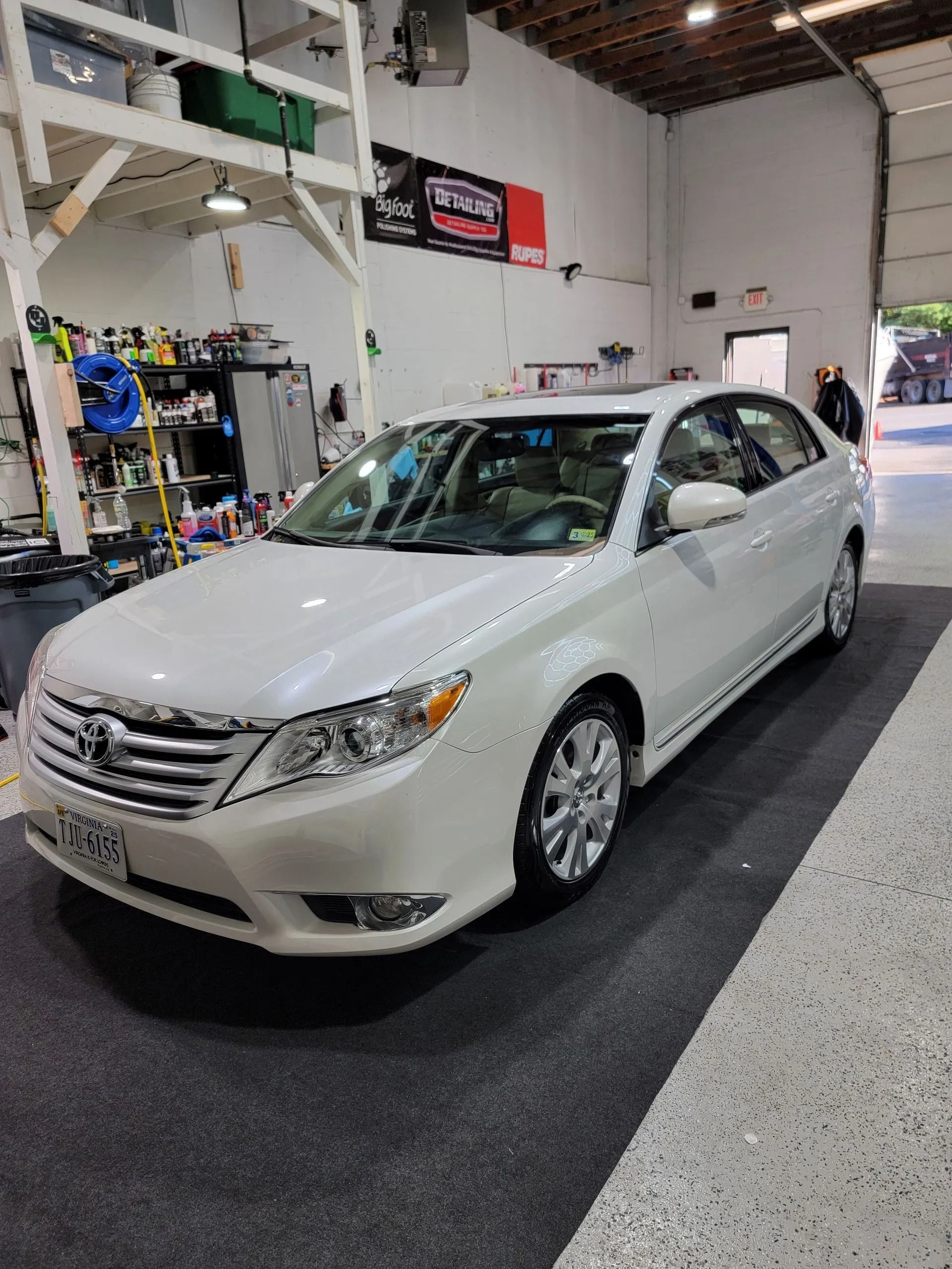 A white Toyota Avalon sedan parked inside a brightly lit auto detailing shop with equipment shelves visible in the back.
