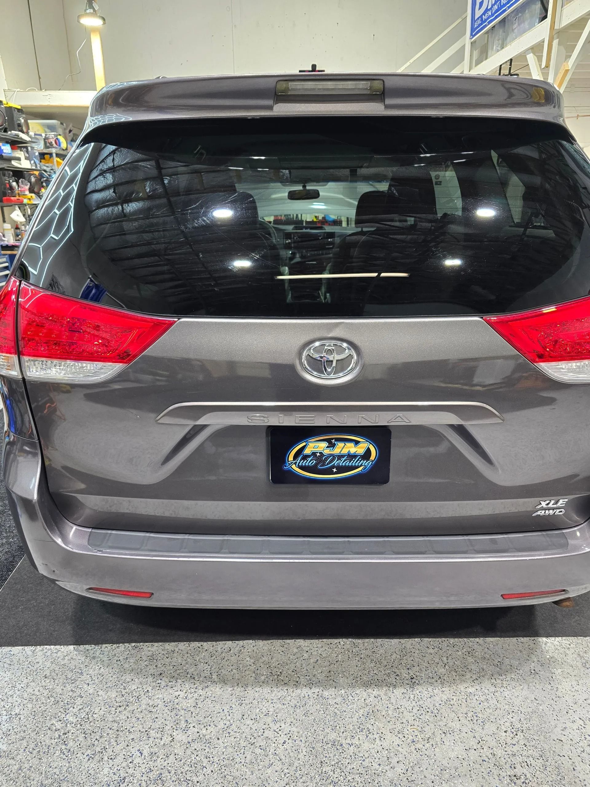 The rear view of a gray Toyota Sienna minivan parked indoors with a dealer license plate.