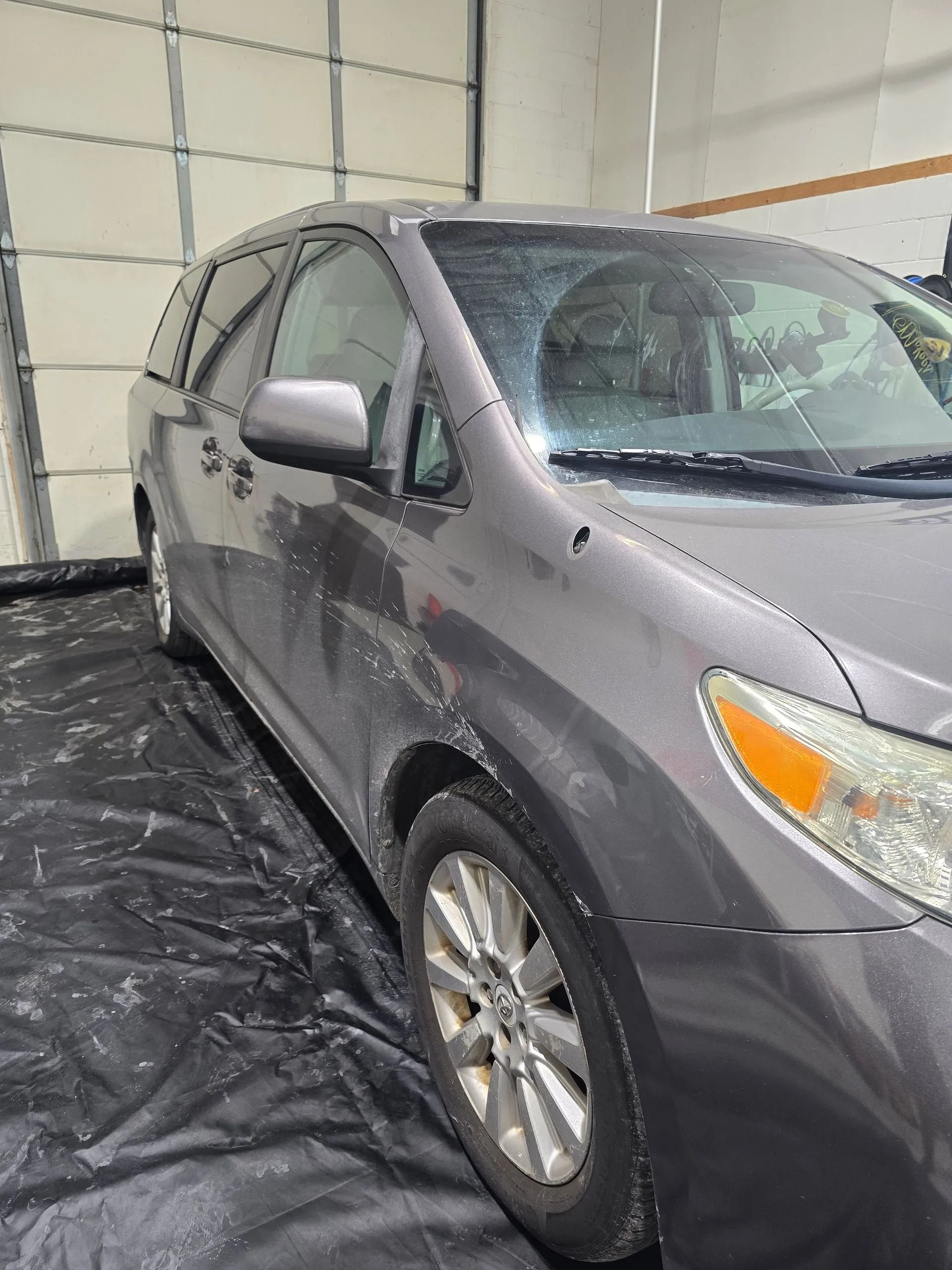 A gray minivan parked indoors on a black protective floor covering.
