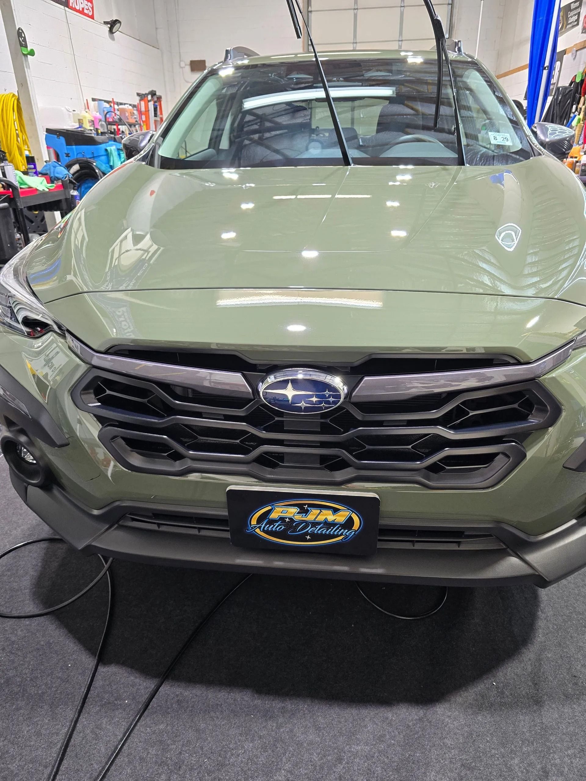 A front view of an olive green Subaru Crosstrek parked inside an auto shop.