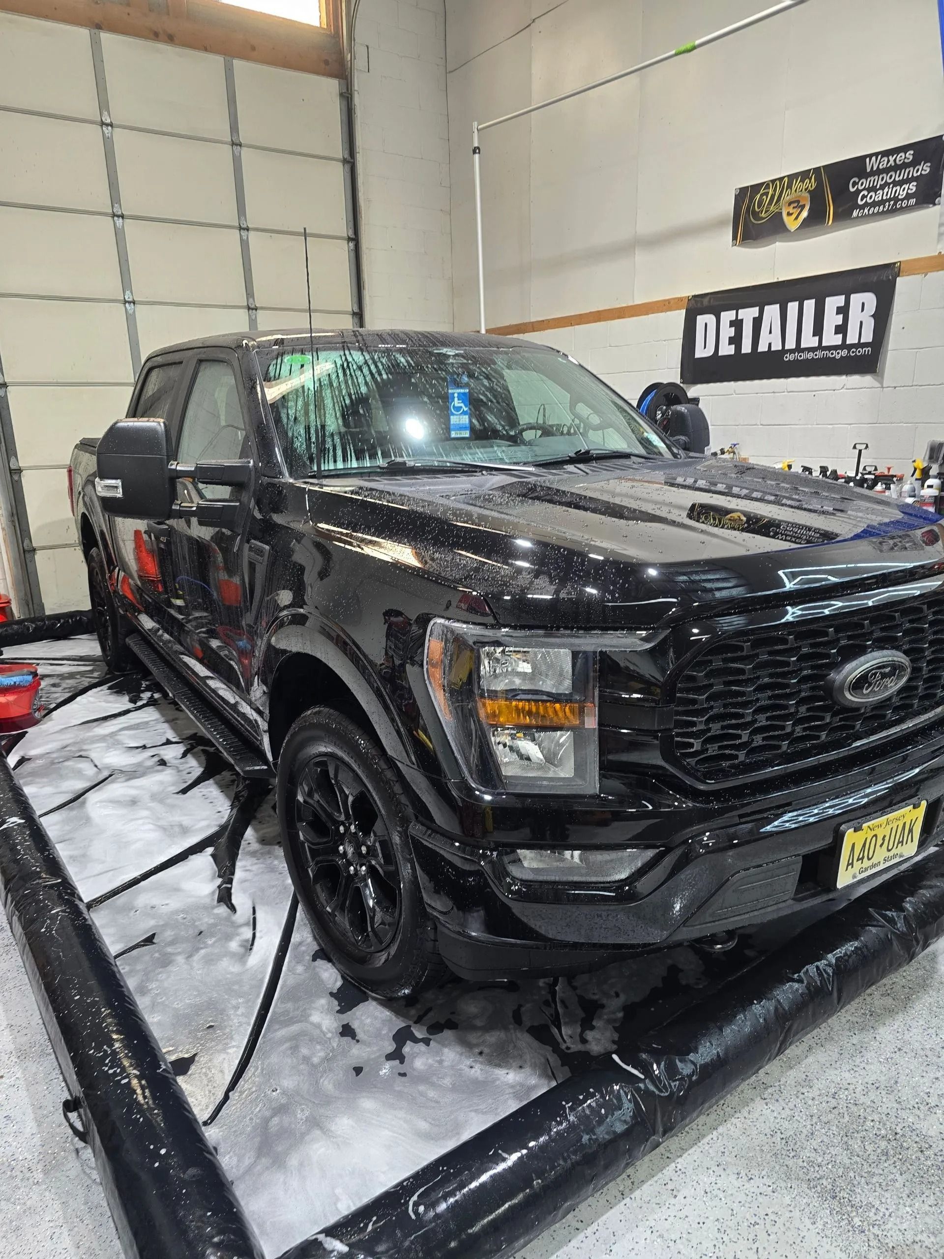 A black Ford F-150 truck parked inside a detailing shop, positioned within a black containment mat.