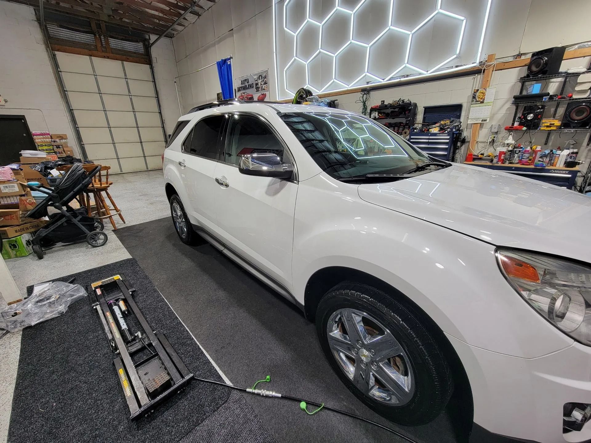 A white SUV parked in a garage with a black equipment rack on the floor next to it.