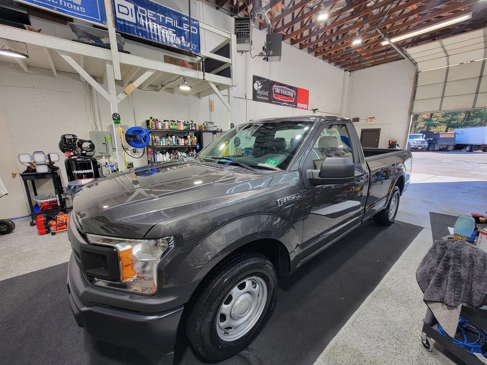A dark gray Ford F-150 regular cab truck parked inside a bright, organized professional automotive detailing shop.