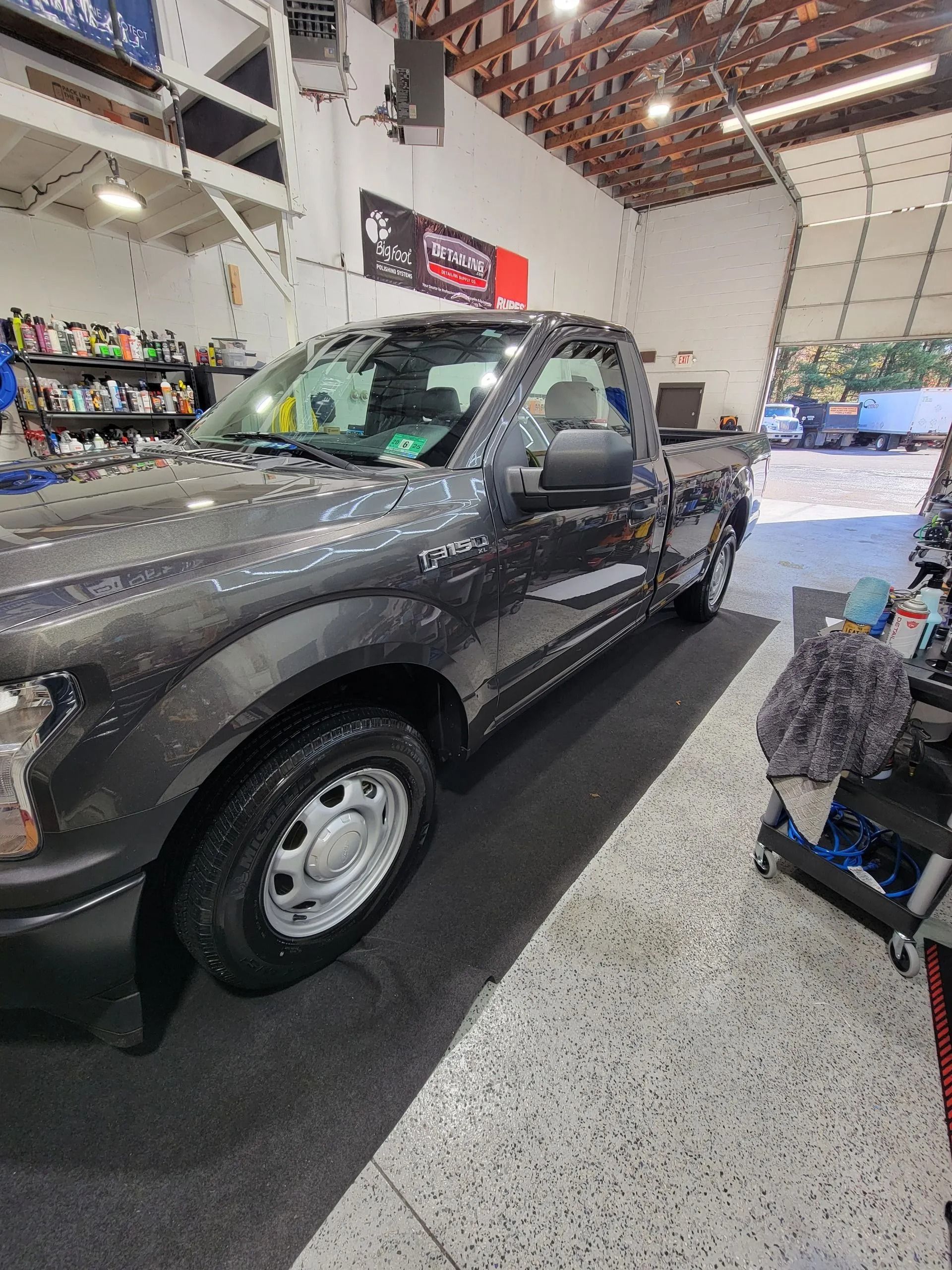 A gray Ford pickup truck parked inside a bright, clean automotive garage with shelves of supplies in the background.