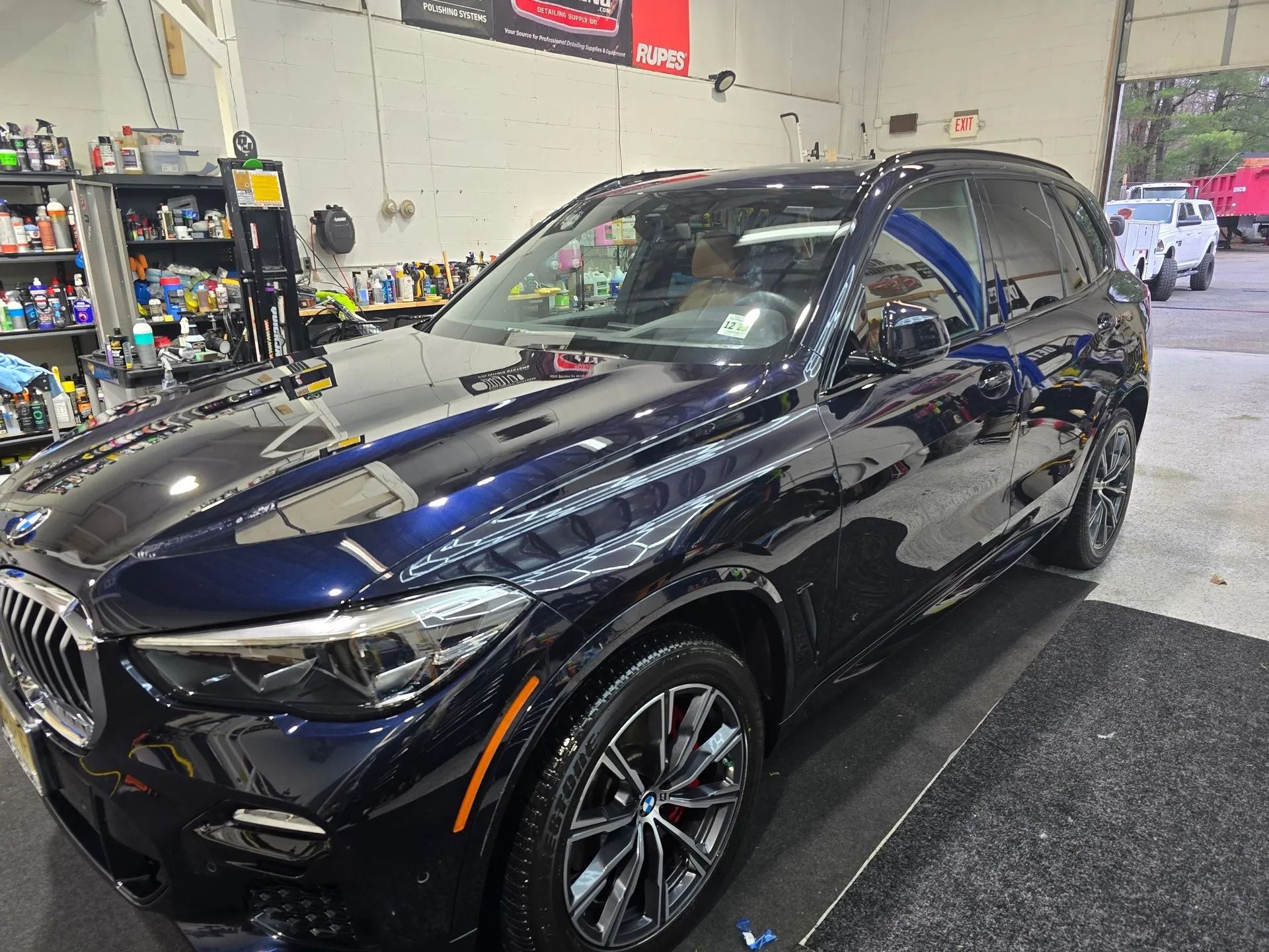 A dark blue BMW SUV parked inside a workshop with automotive supplies on shelves in the background.