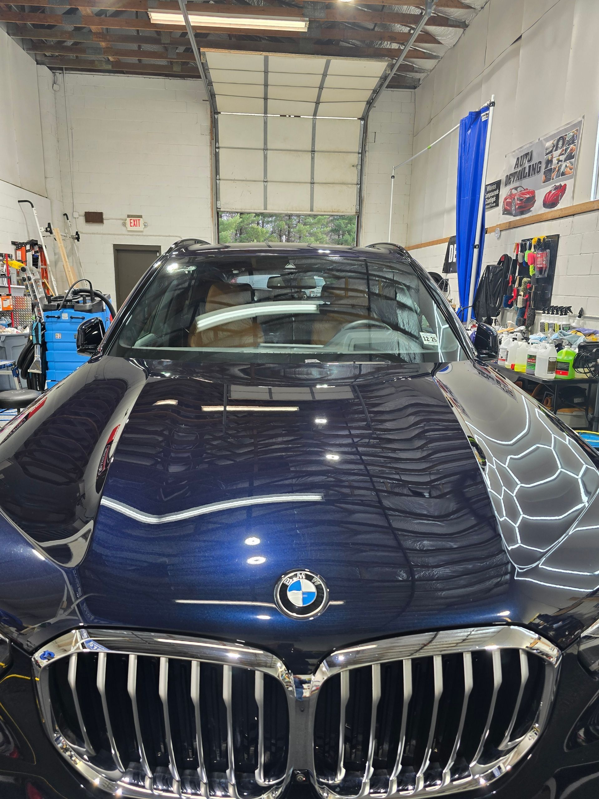 A dark blue BMW SUV parked inside a workshop with large front grilles reflecting shop lights.