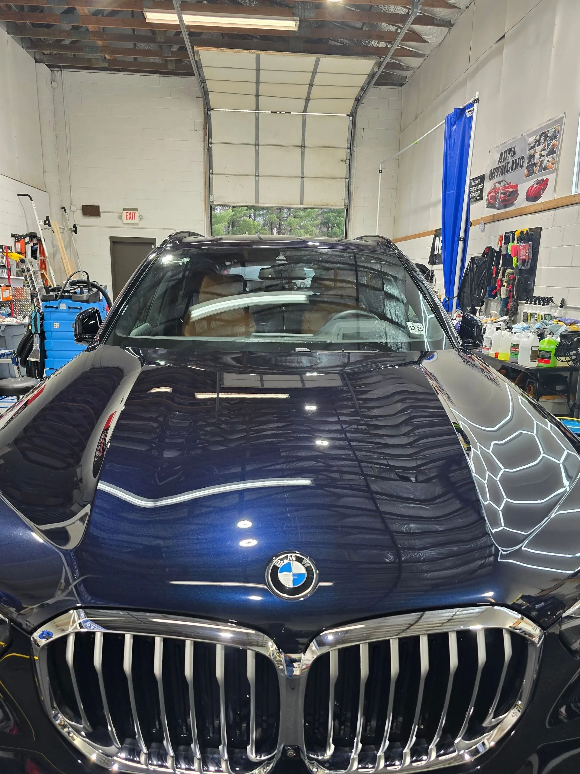 A dark blue BMW SUV parked inside a brightly lit auto shop with a large garage door in the background.