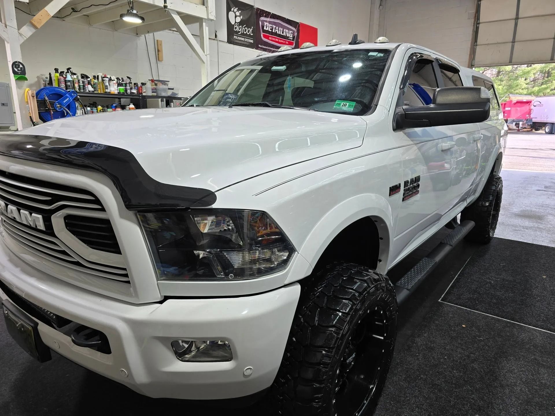 A white Ram pickup truck with black wheels and a hood deflector parked inside a garage.