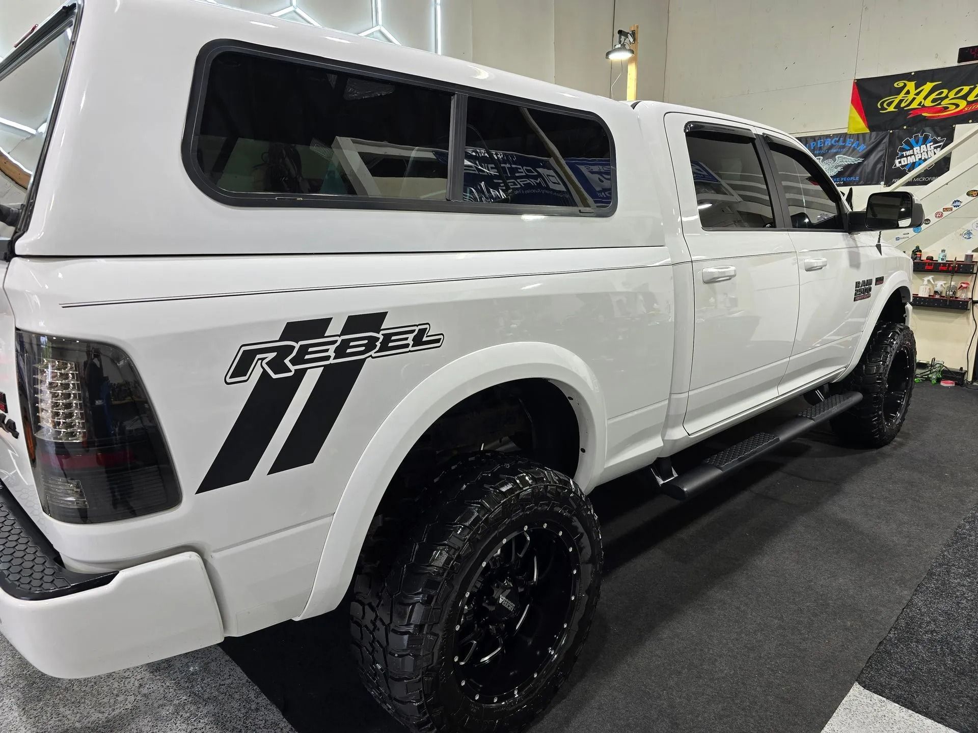A white Ram Rebel pickup truck with a camper shell, black wheels, and a black 