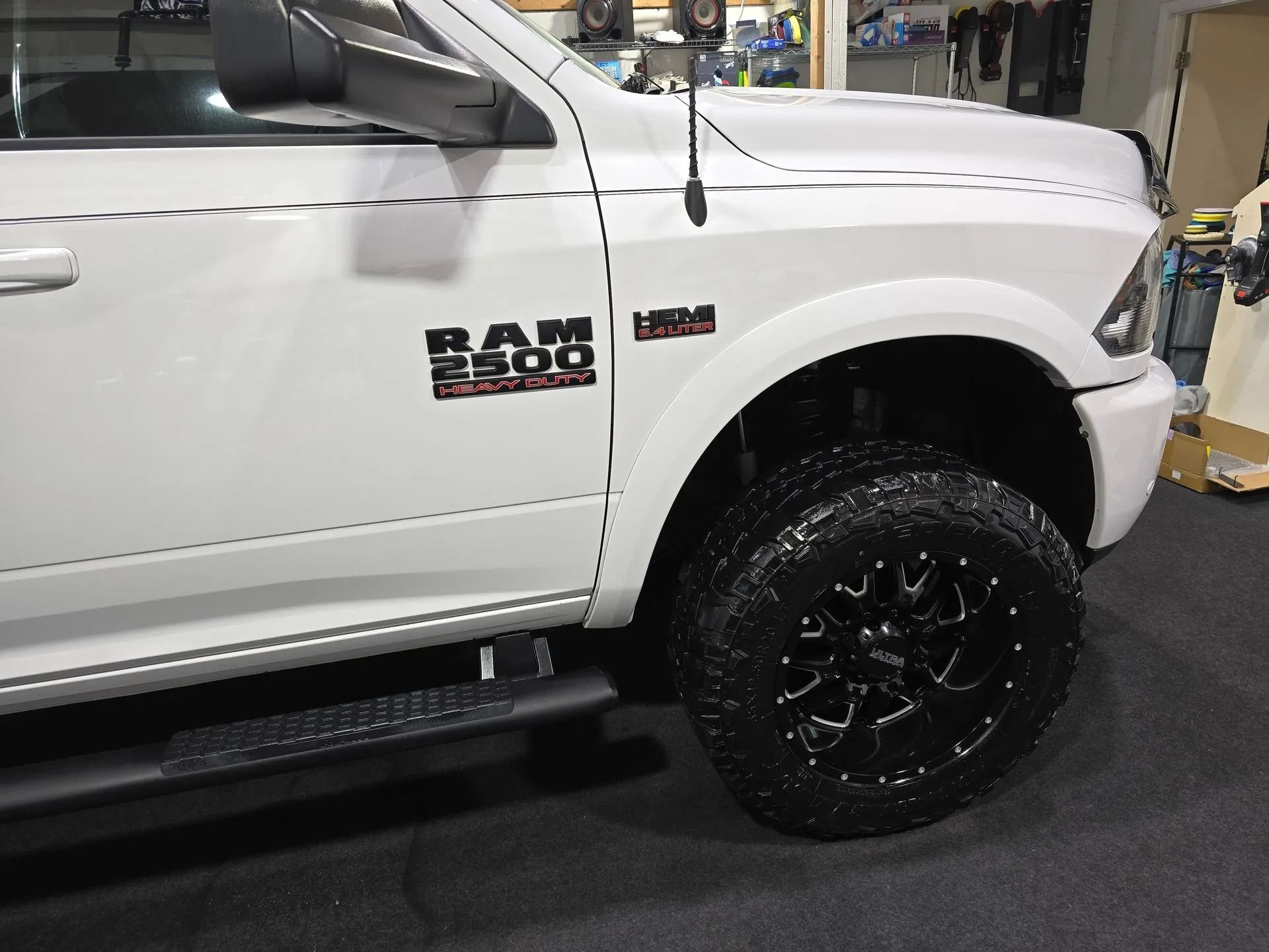 Close-up side view of a white Ram 2500 heavy-duty truck with custom black wheels, parked in a garage.