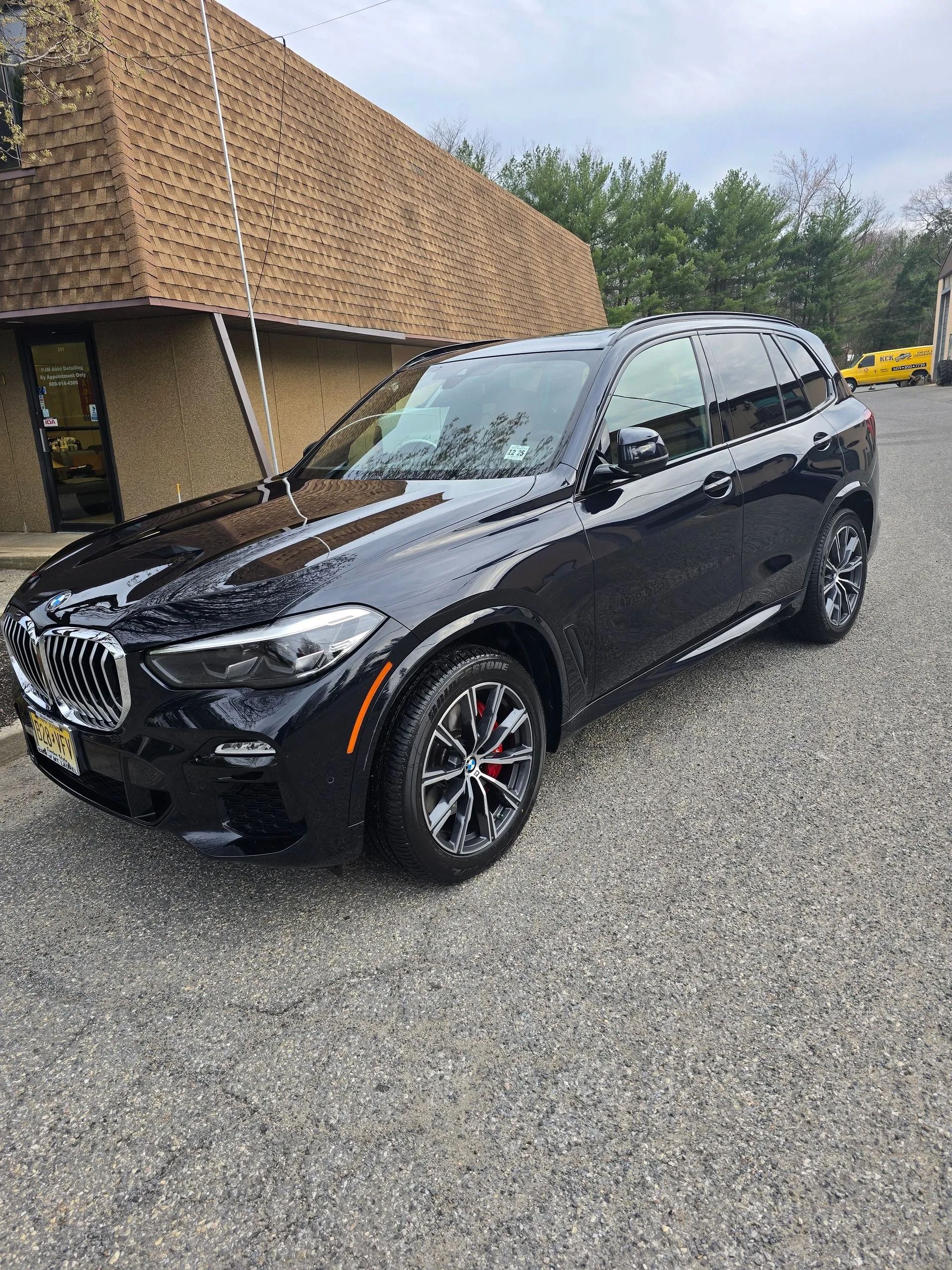 A black BMW SUV parked on a gravel lot in front of a building with a shingled roof.