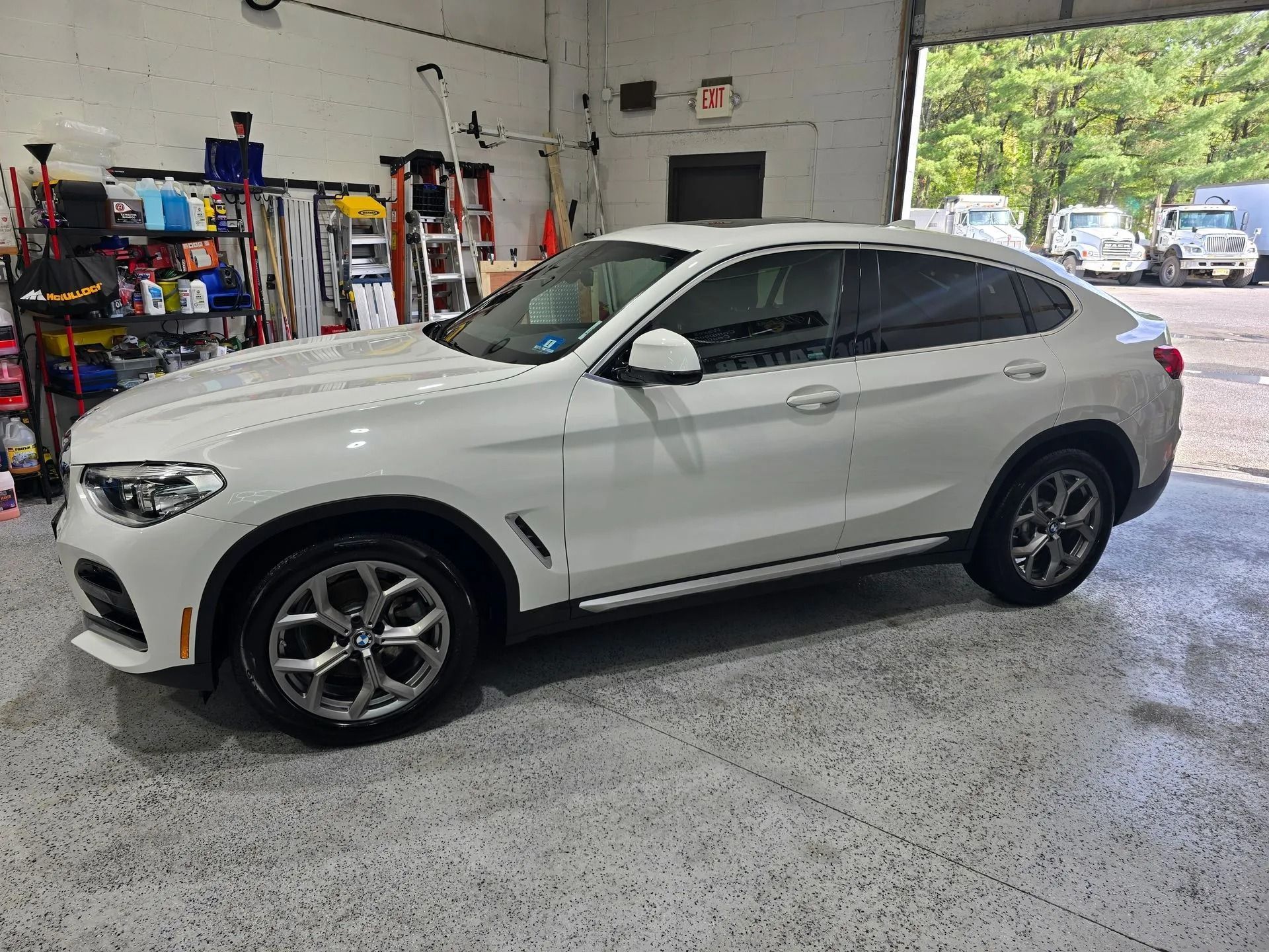 A white BMW X4 SUV parked inside a well-lit auto garage with concrete floors.