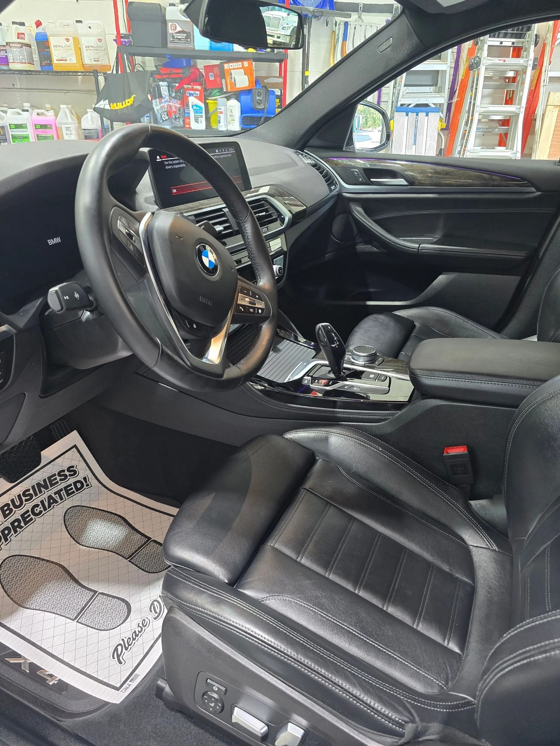 Interior view of a modern BMW featuring black leather seats, a steering wheel with the BMW emblem, and a paper floor mat.