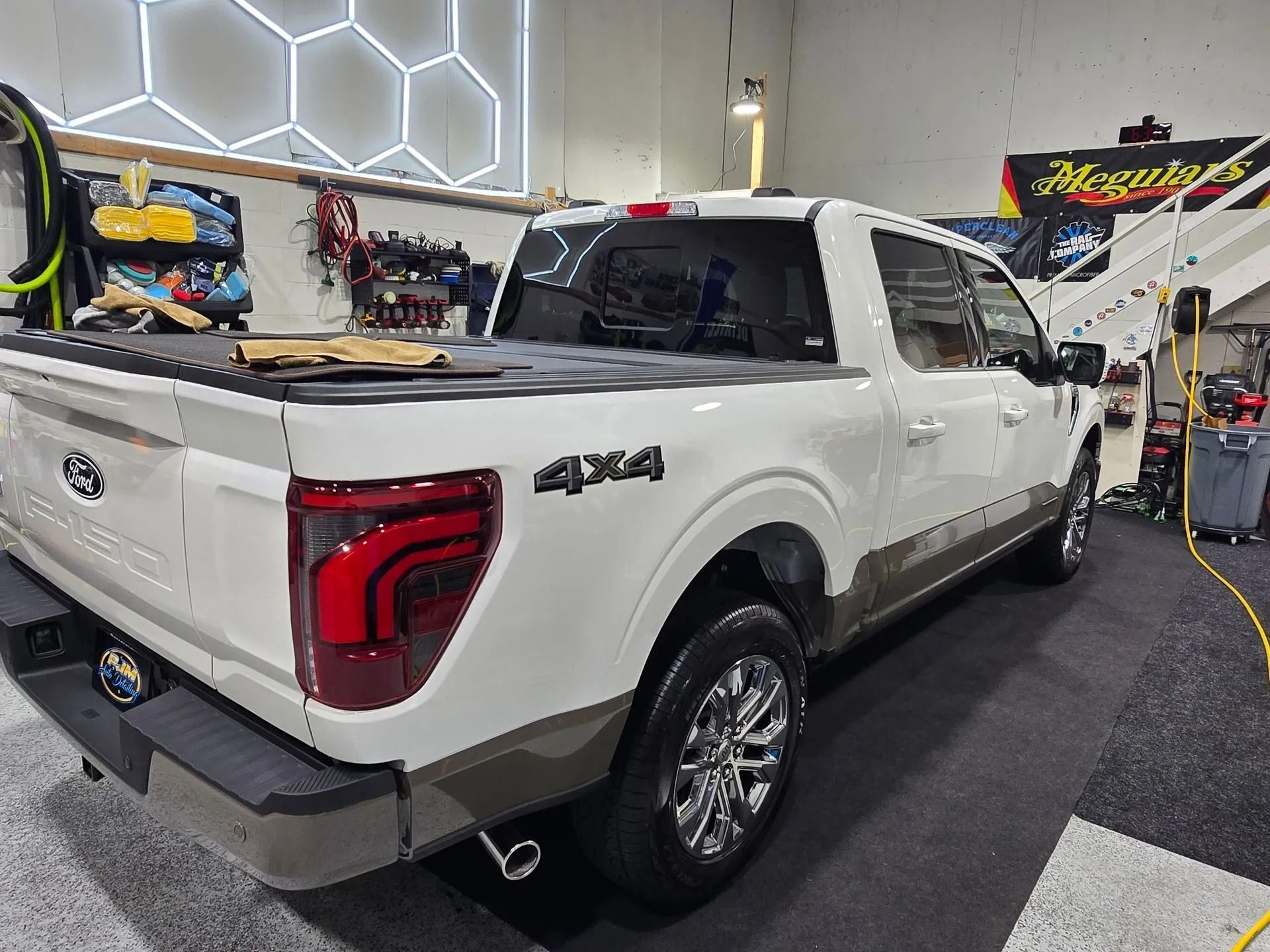 A white Ford F-150 4x4 pickup truck with a two-tone tan lower body parked inside a garage.