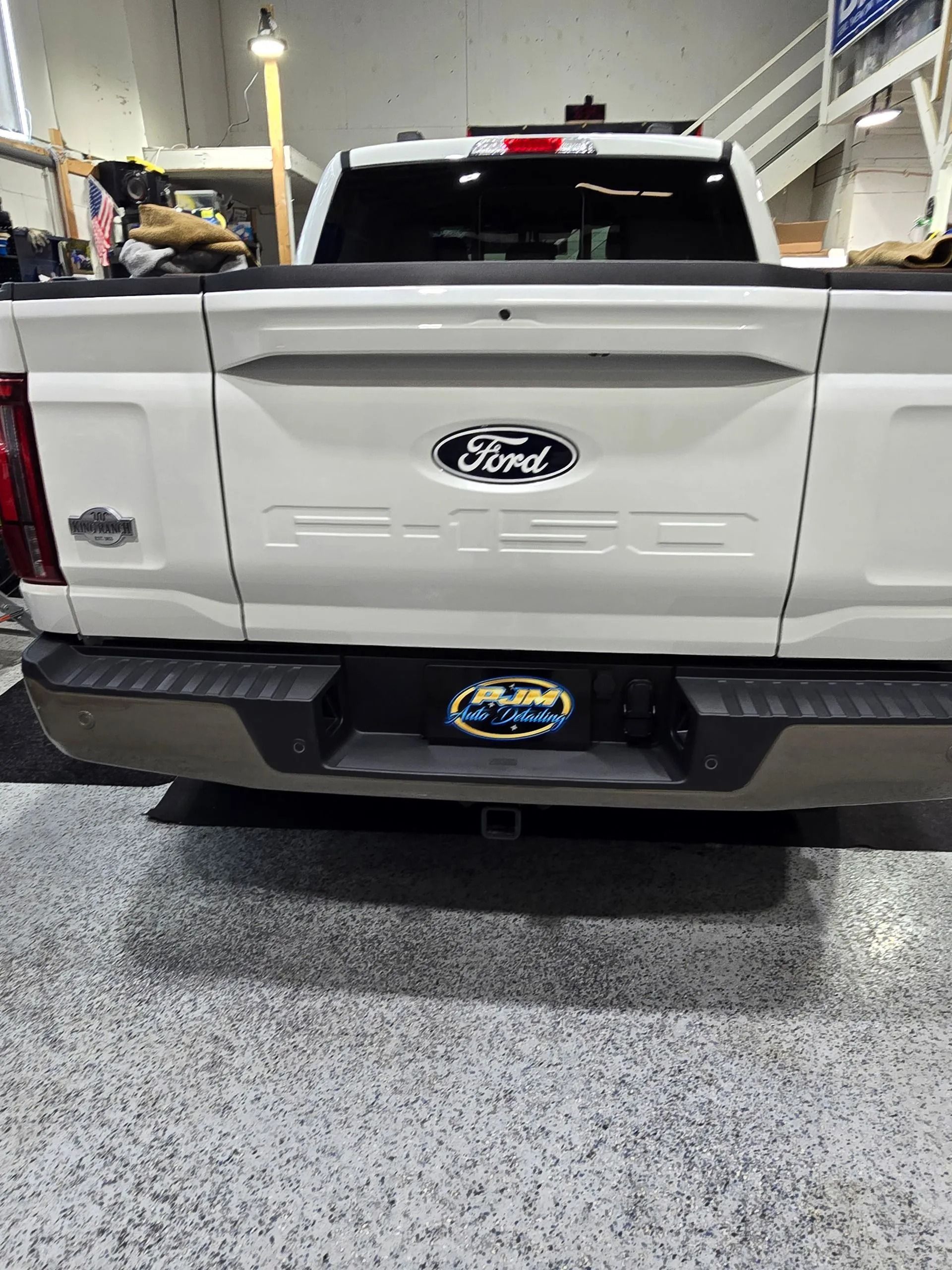 Rear view of a white Ford F-150 truck with a dark bumper, parked indoors on a speckled floor.