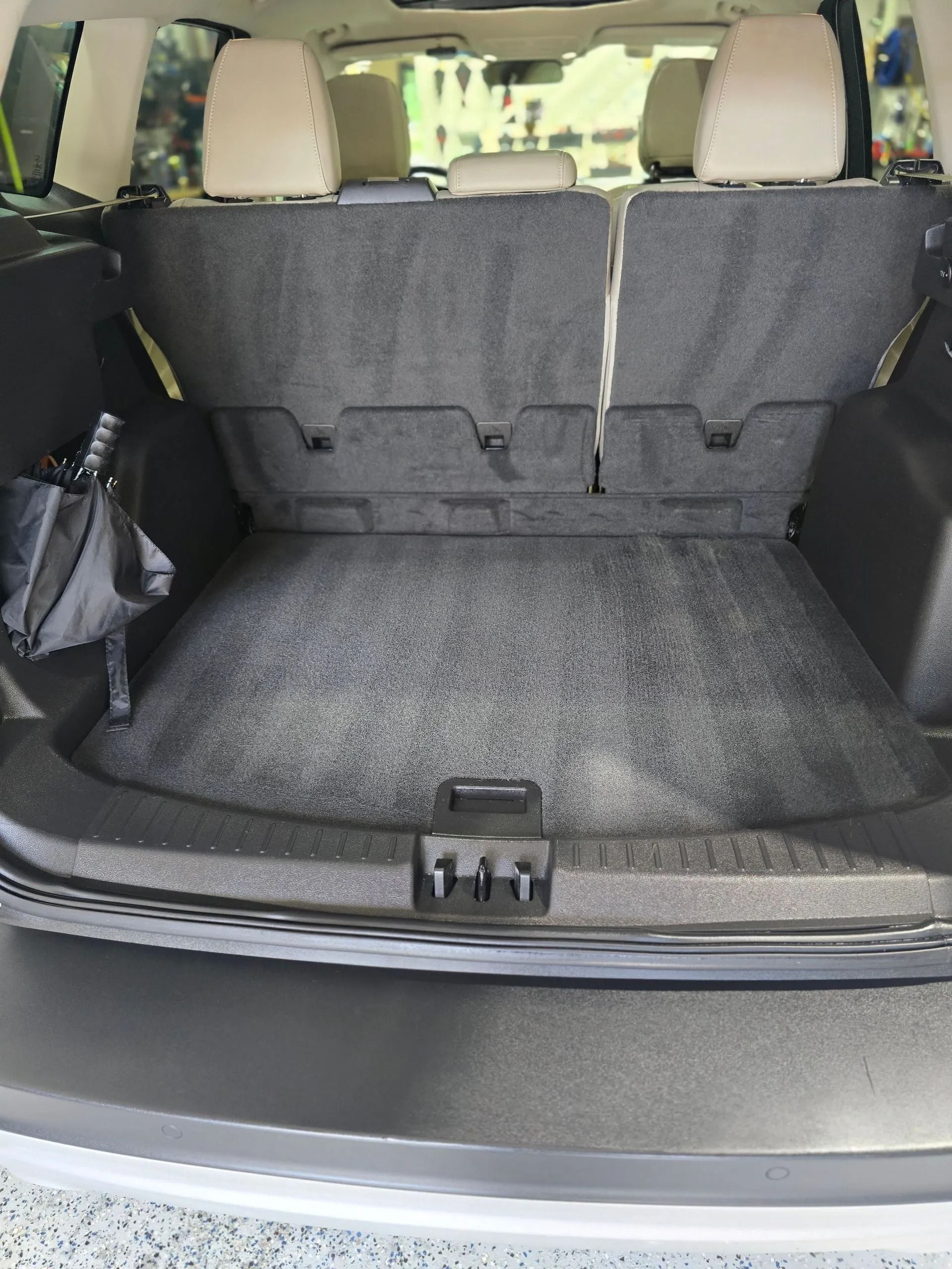 Open trunk of an SUV showing folded rear seats, gray carpeted floor, and a black bag on the left side.