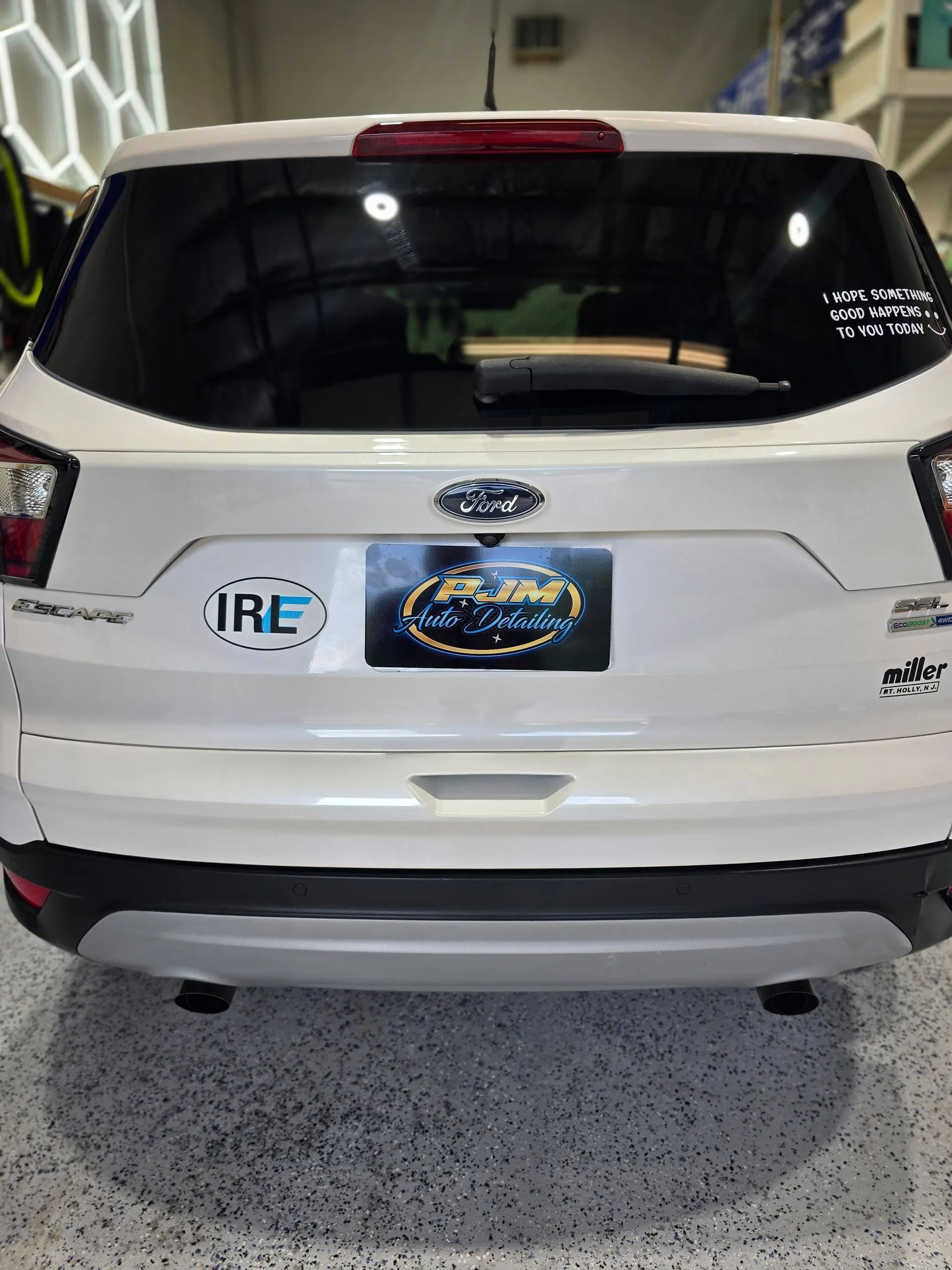 A white Ford Escape parked indoors, featuring branding stickers on the rear hatch and a black and white license plate.