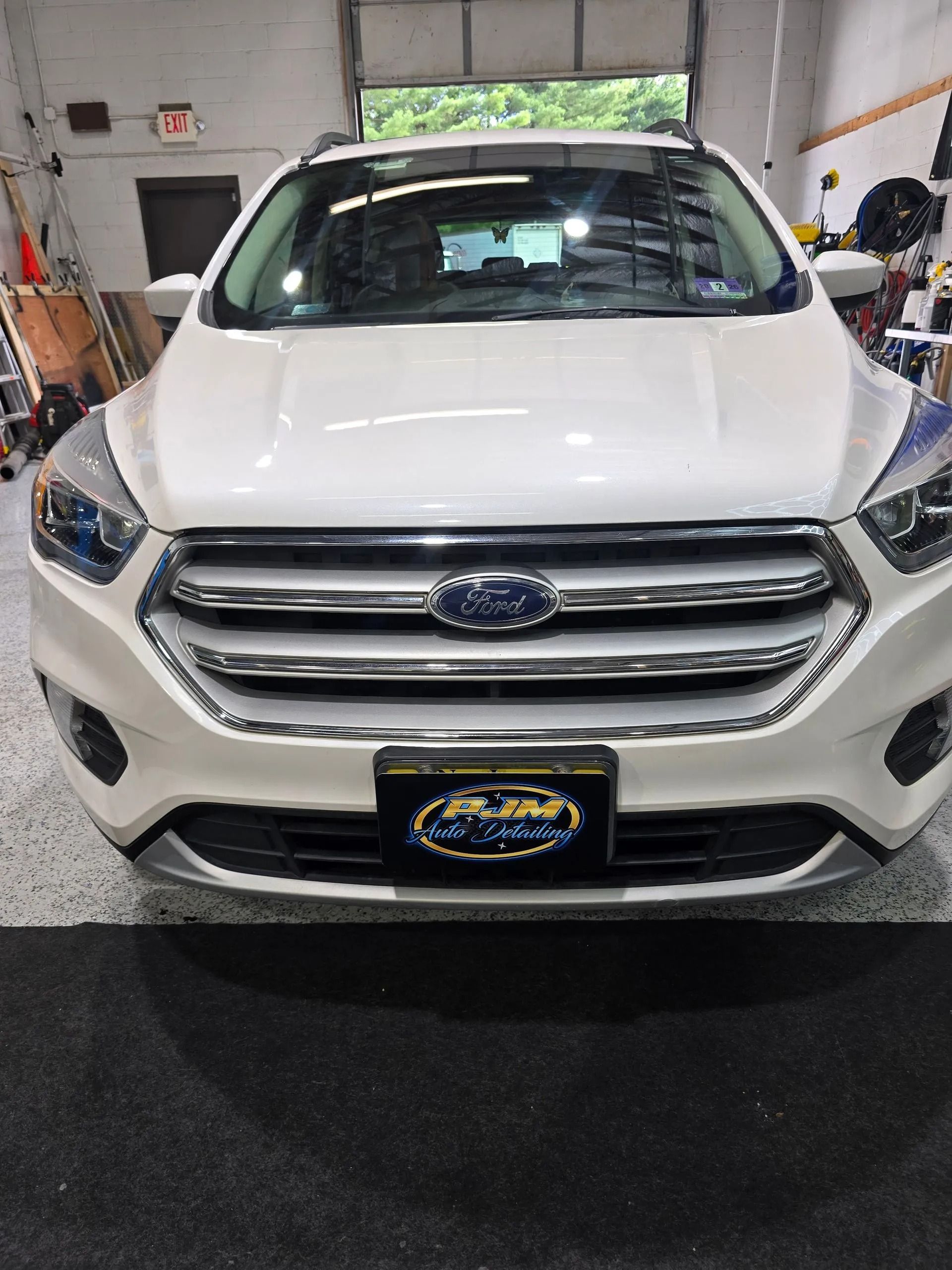 A white Ford Escape SUV parked in a garage, facing forward with a branded license plate on the front bumper.