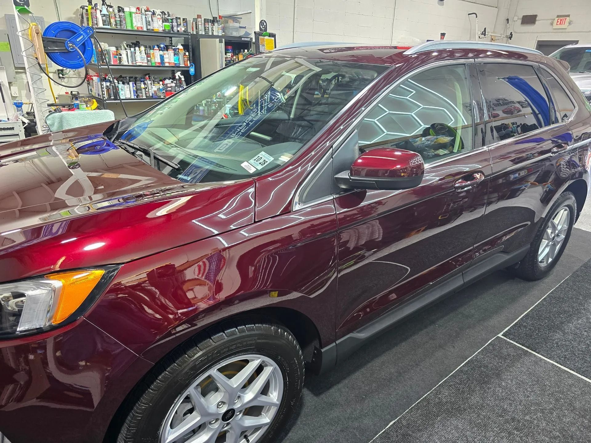 A shiny dark red SUV parked in a garage with shelves of car supplies in the background.