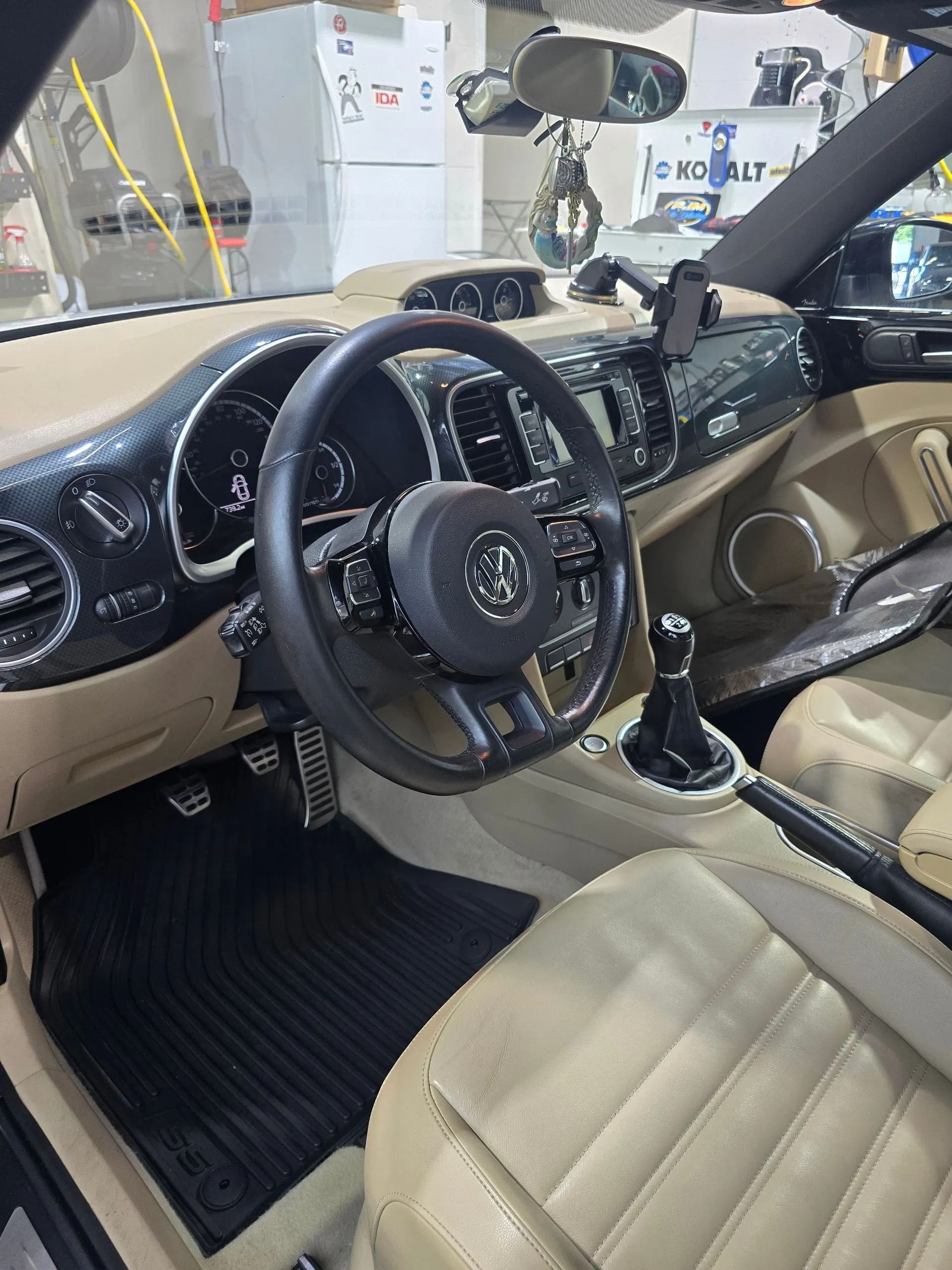 A view inside a car's cockpit, showing a black steering wheel, tan leather seats, and a black floor mat.