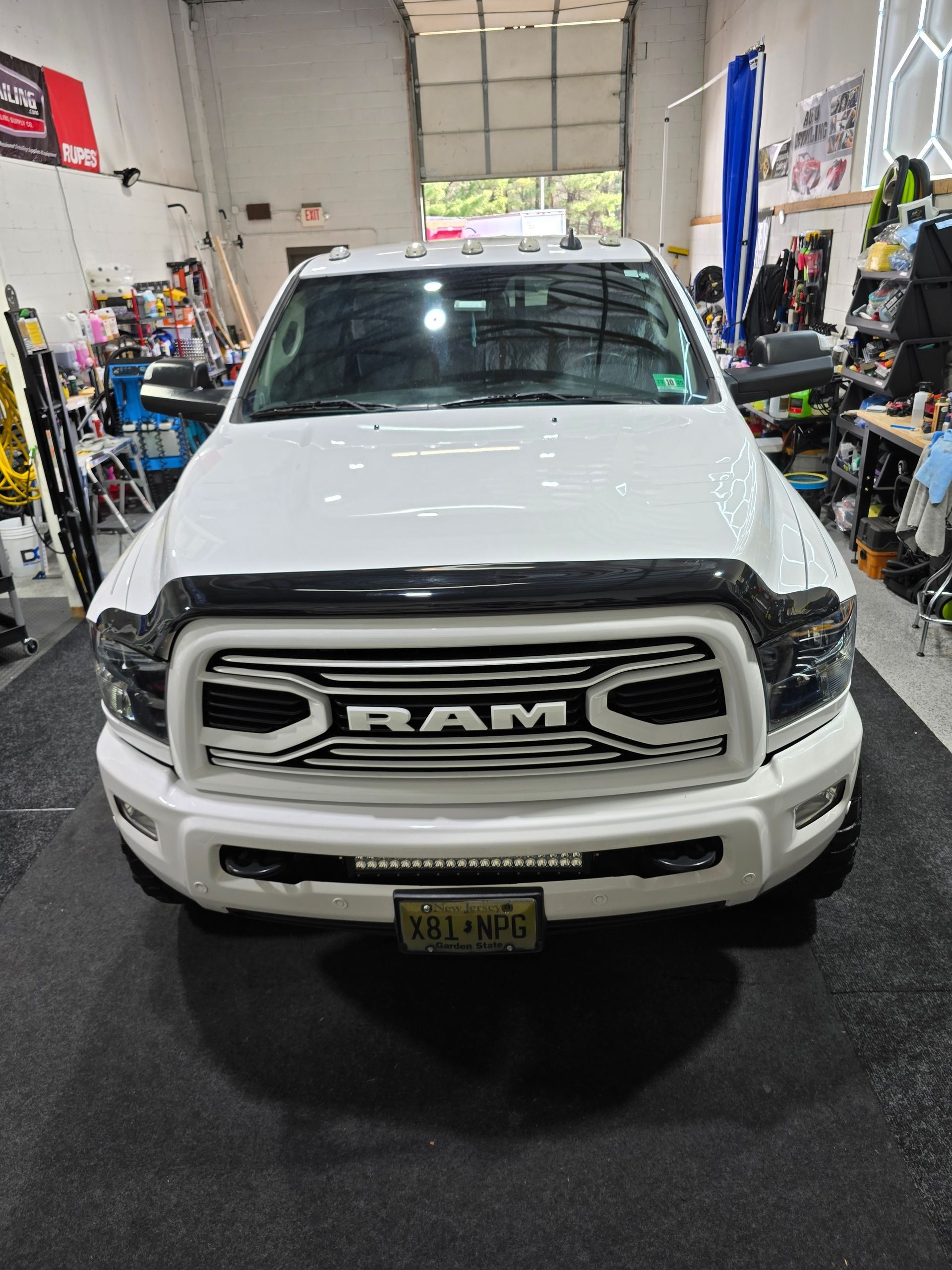 A white RAM pickup truck parked in a garage, featuring a large, stylized RAM logo on the front grille.