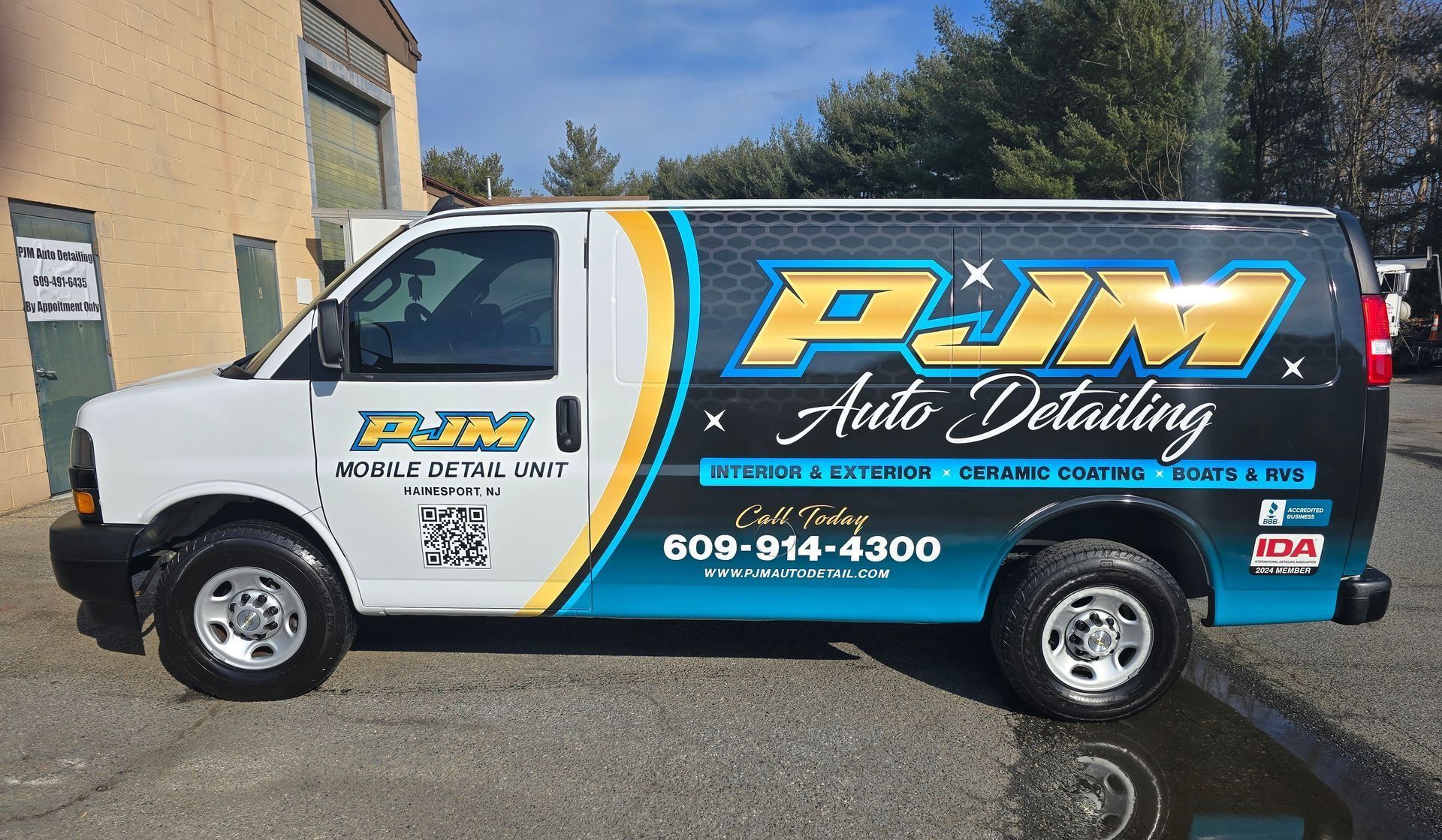 A white and black PJM Auto Detailing van parked outdoors with blue accents, branding, and a contact phone number.