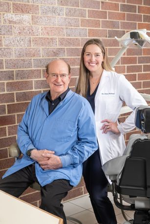 Dentist and hygienist in a clinic, smiling beside a dental chair.
