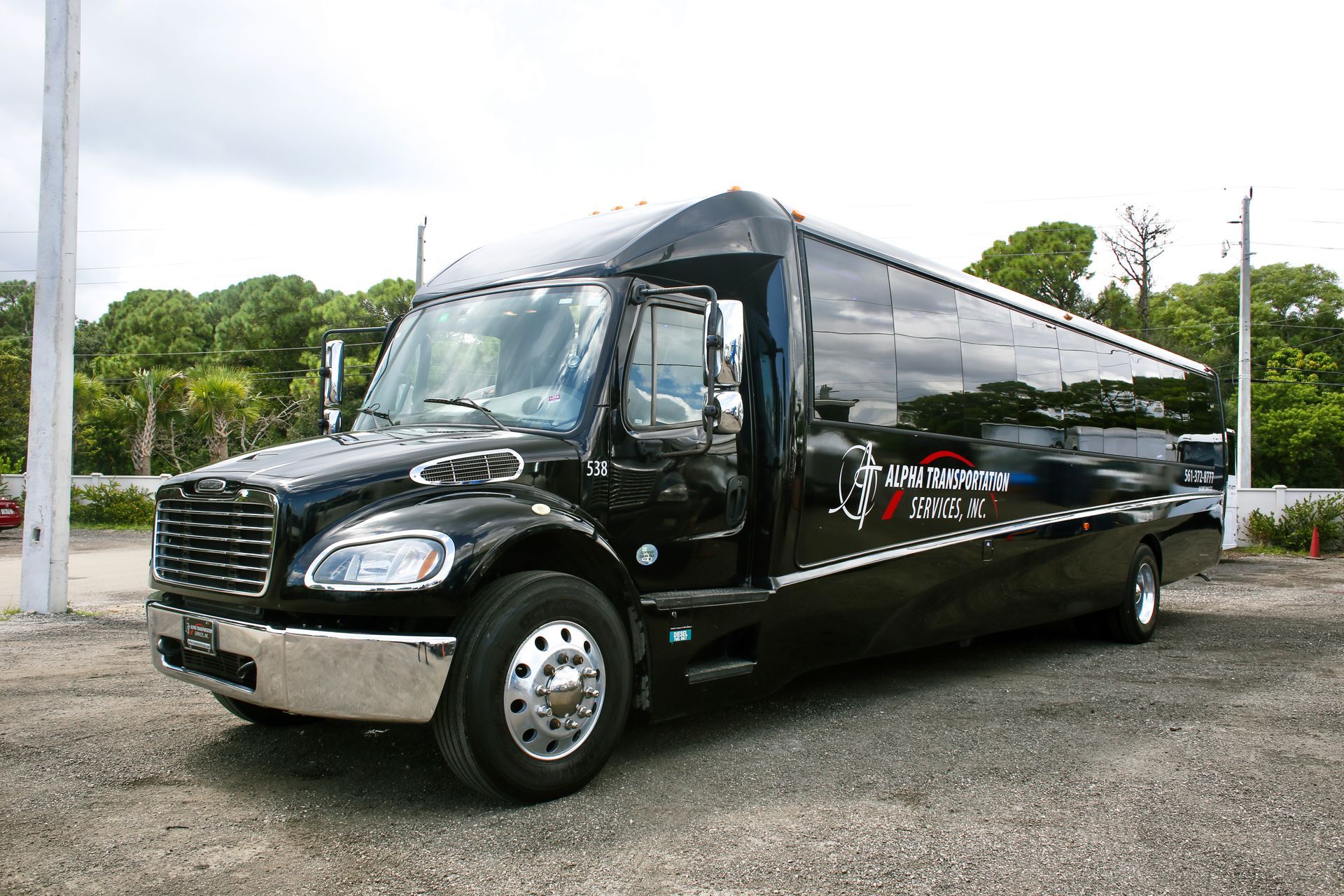 Black charter bus parked on a gravel lot, side view with red and white logo.