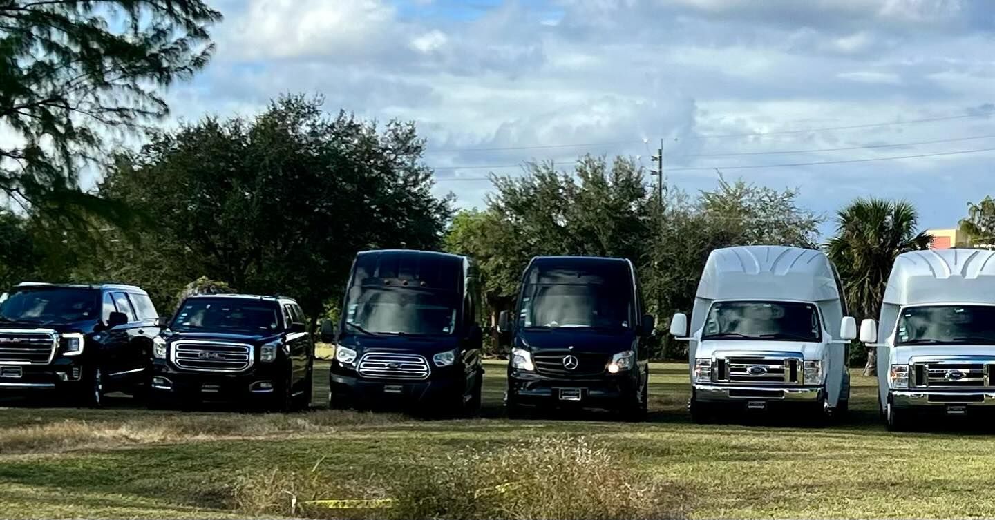 Six vans and SUVs parked in a grassy field under a cloudy sky.
