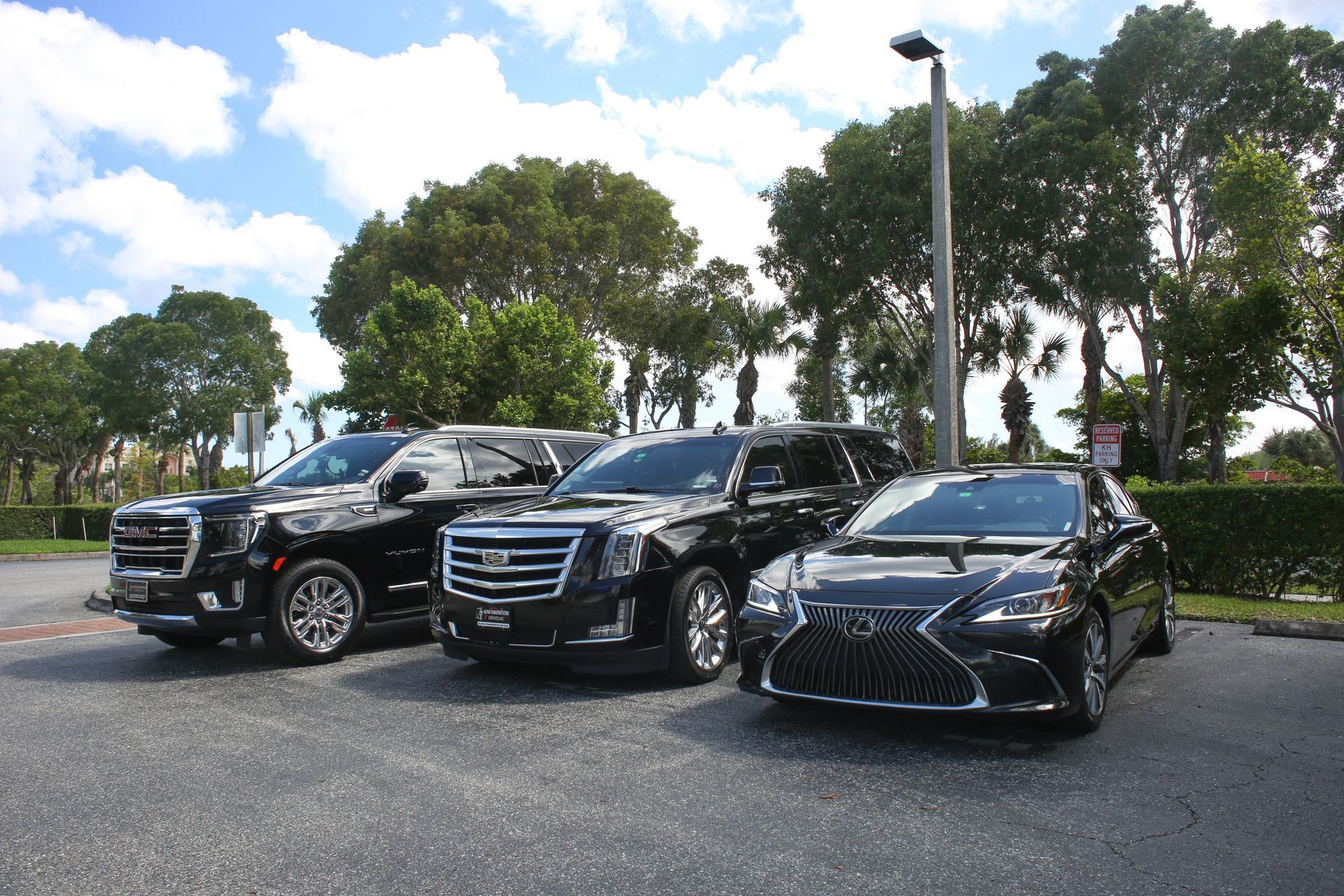 Three black SUVs parked outdoors on a sunny paved lot with trees in the background
