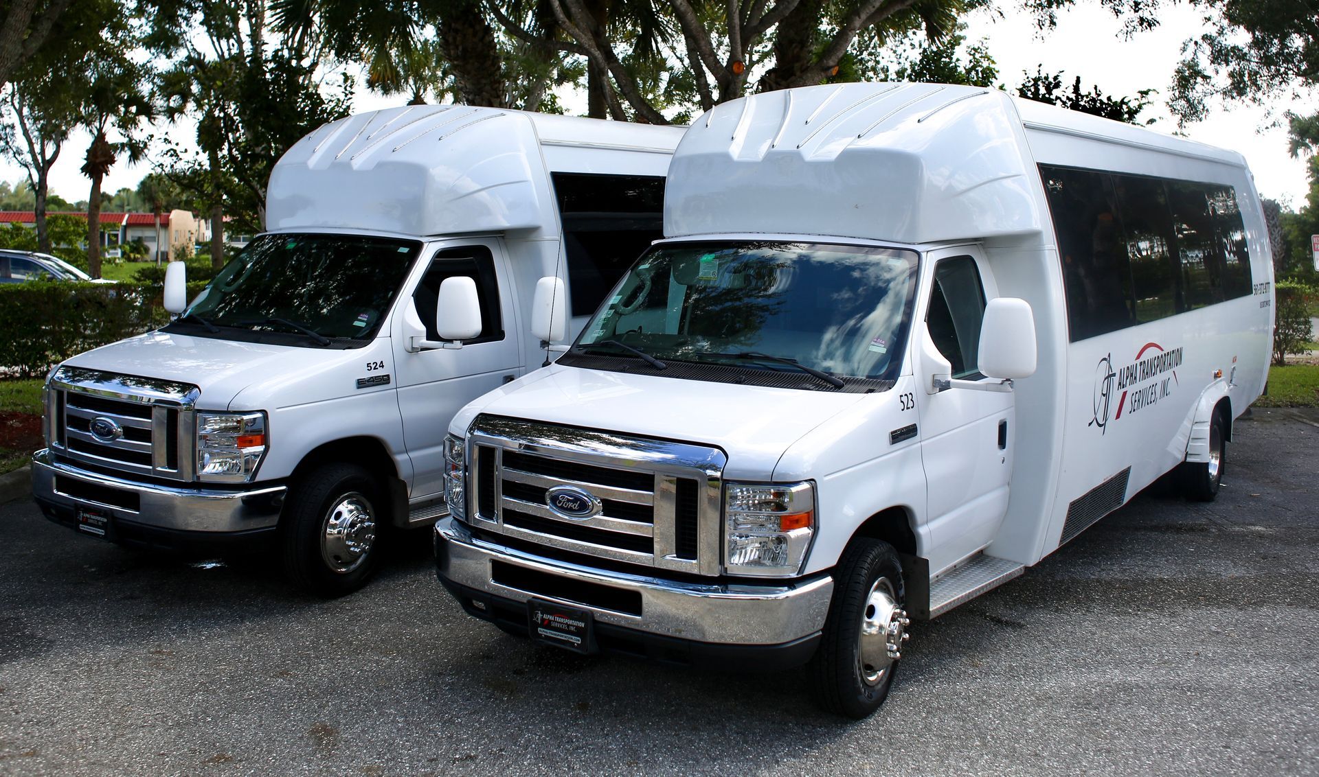 Two white shuttle buses parked on a gravel lot under trees