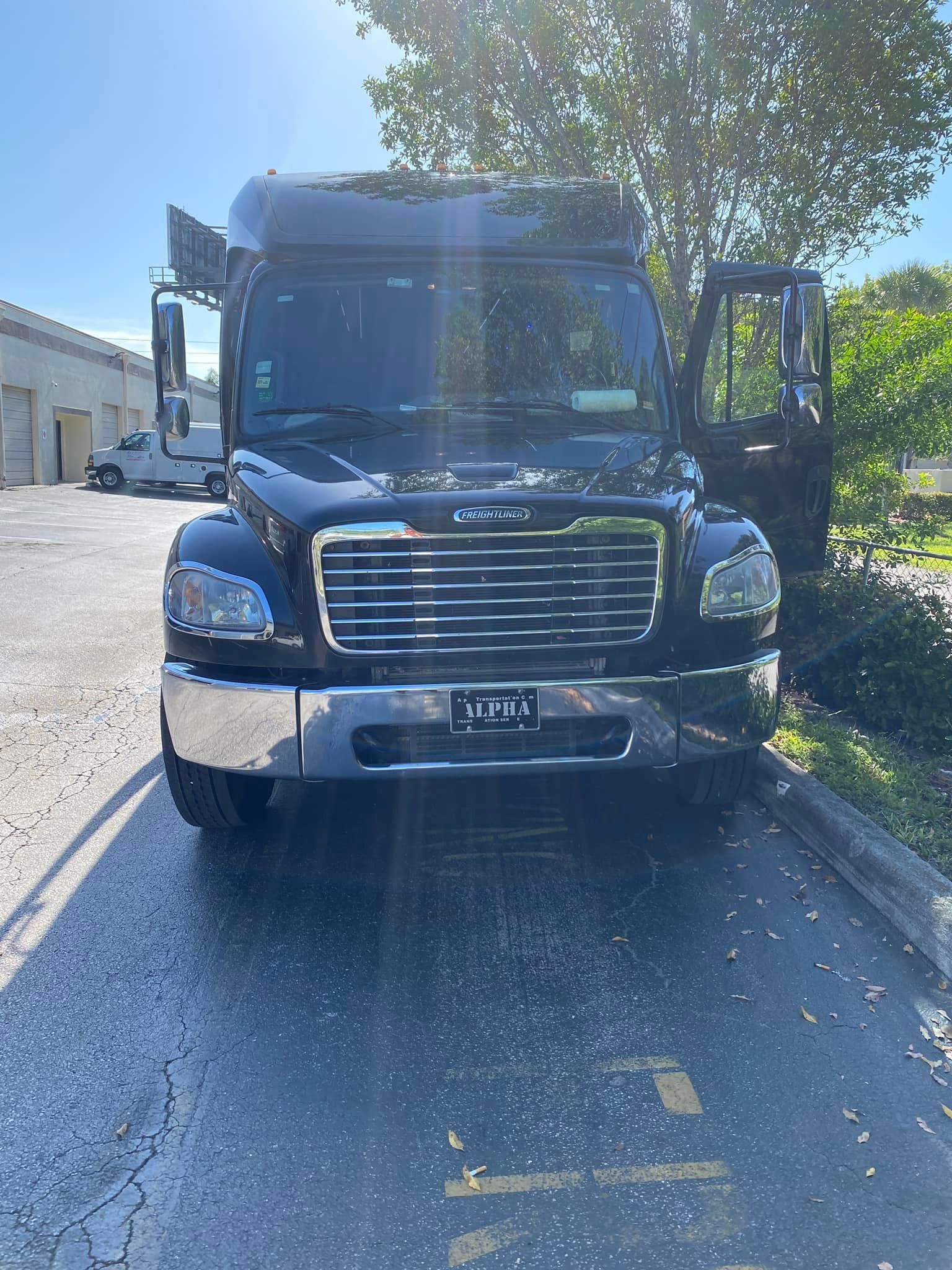 Blue semi-truck parked on a sunlit street with trees and buildings nearby, front view, driver door open