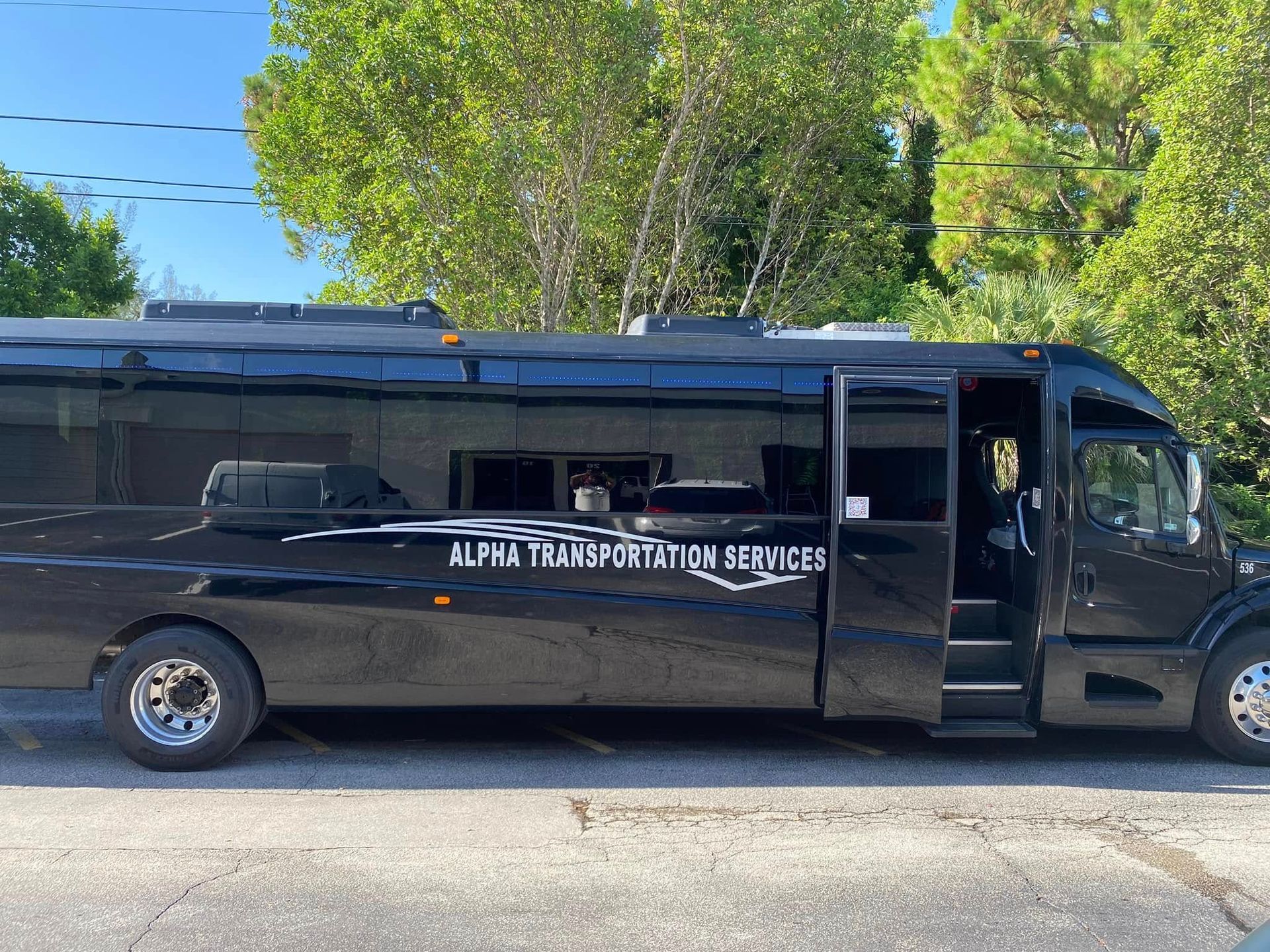 Black shuttle van with white lettering parked on a street beside trees and power lines.