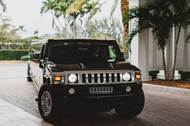 Black Hummer SUV parked on a palm-lined driveway near a building entrance