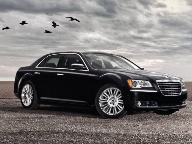 Black luxury sedan on a gravel road under a cloudy sky with birds overhead