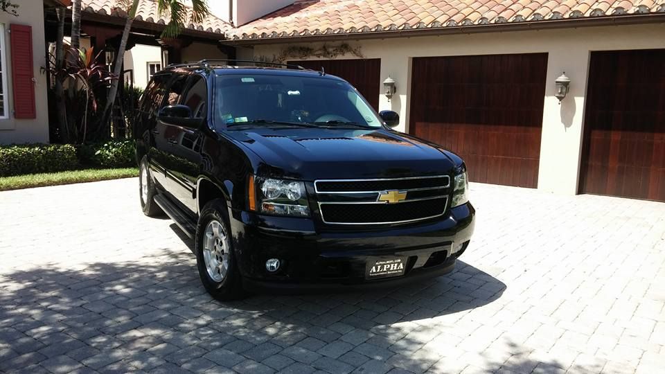 Black SUV parked in a sunlit driveway in front of a house with a tiled roof