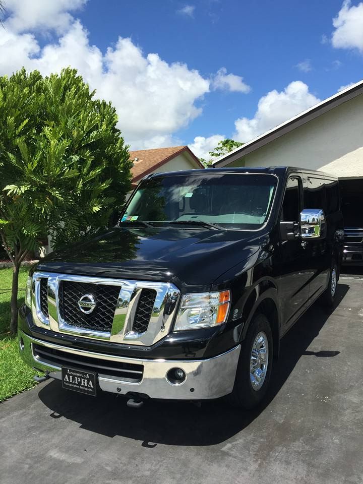 Black Nissan pickup truck parked in a driveway beside a green lawn and house under a blue sky.