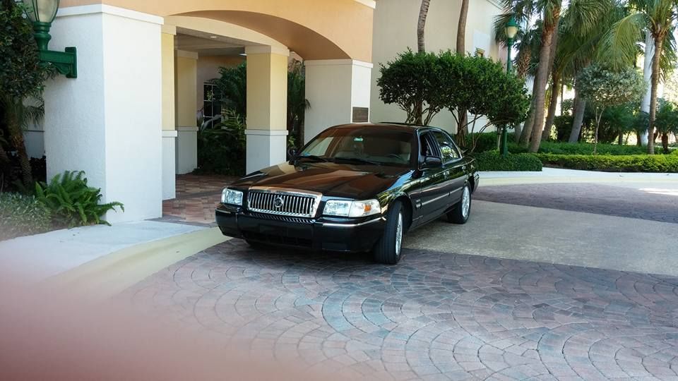 Black sedan parked under a beige building entrance with palm trees nearby