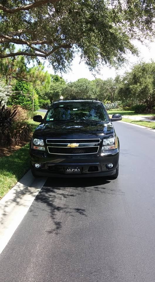 Black SUV parked on a tree-lined suburban street beside the curb.
