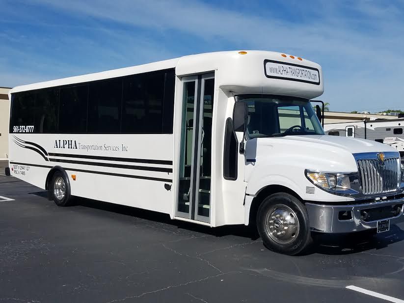 White shuttle bus parked on asphalt under a blue sky, side door open.