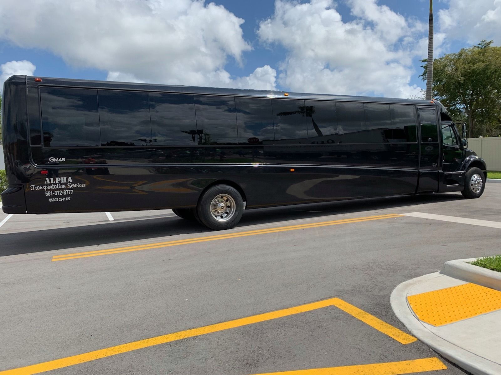 Long black limousine-style bus parked on a street near a curb under a partly cloudy sky