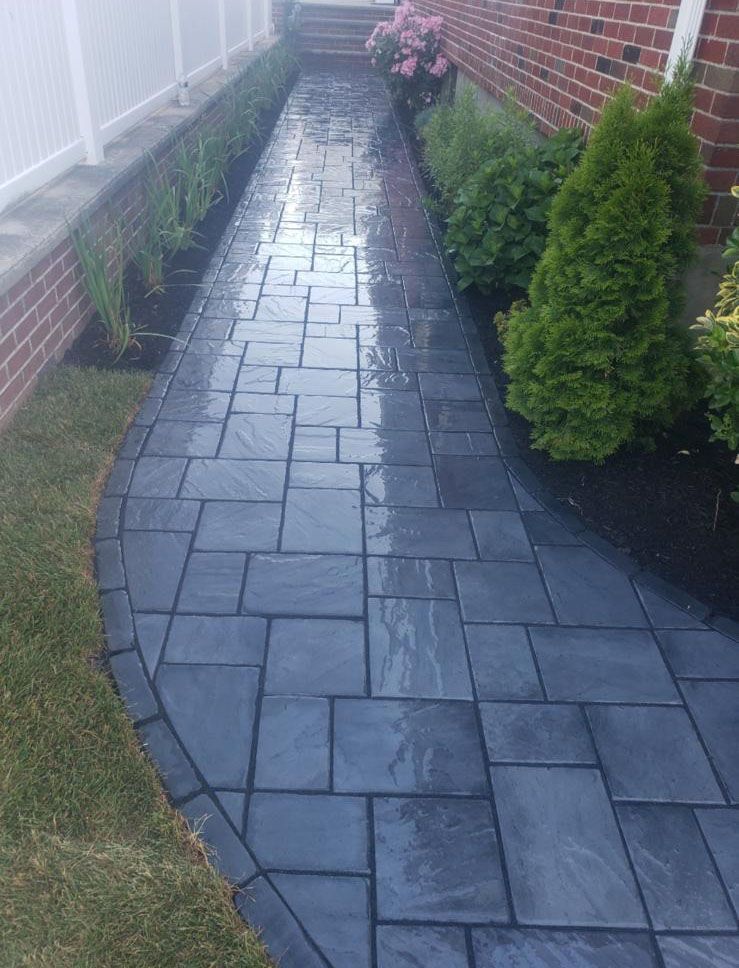 A brick walkway leading to a house with a white fence.