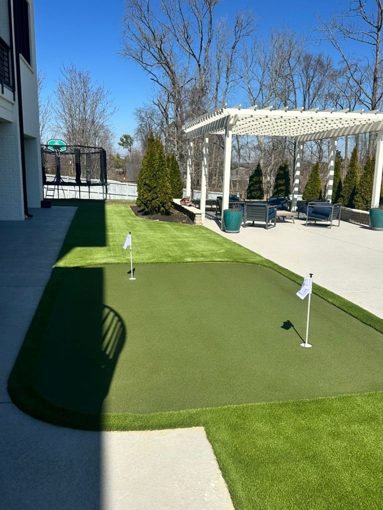 Artificial turf putting green next to a patio with seating; sunny day.