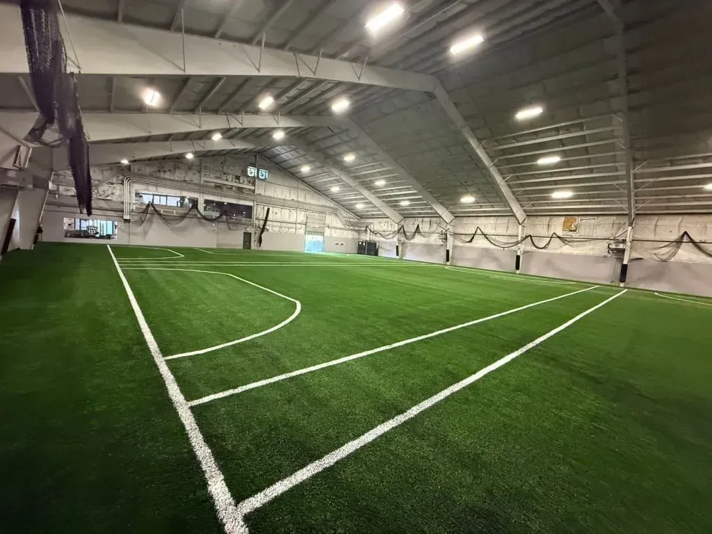 Indoor soccer field with green turf, white lines, and bright overhead lights.