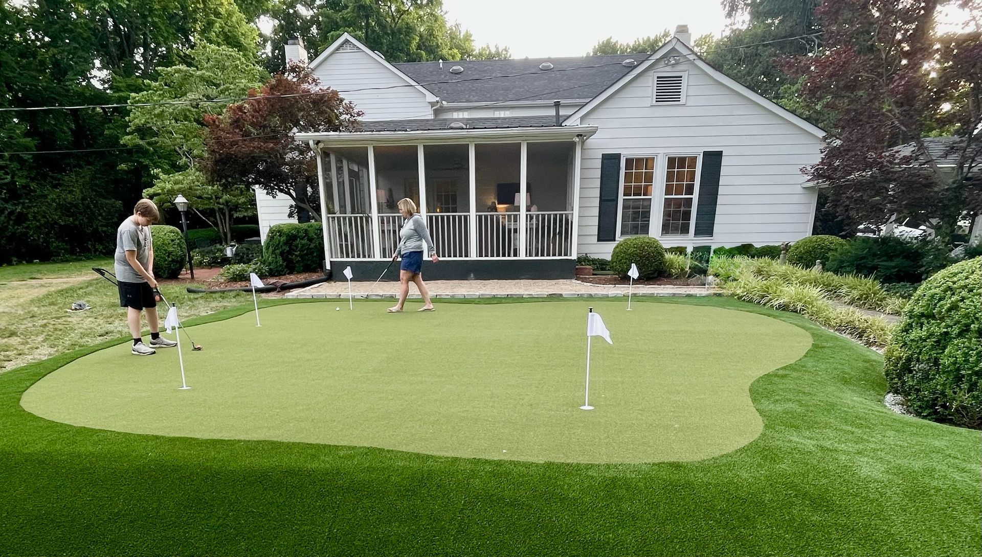 Two people putting on a backyard putting green, with a house in the background.